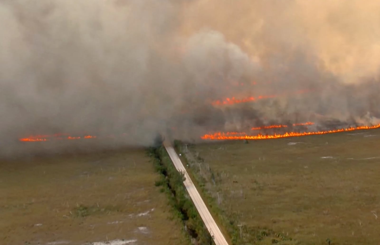 In this image taken from video provided by WSVN-TV, a brush fire burns across and over Card Sound Road, the only other road connecting the Keys to Florida City on the mainland, as it remains closed Tuesday, March 18, 2025, south of Dade County, Fla. (WSVN-TV via AP)