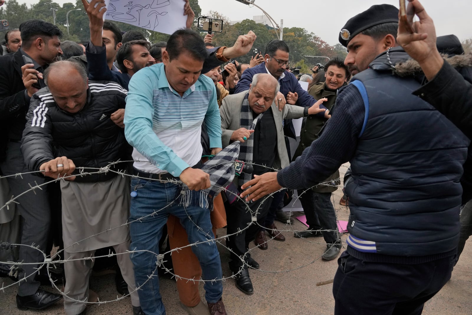 Journalists remove a barbed-wire wire placed by police to stop them for marching toward parliament in Islamabad, Pakistan, Tuesday, Jan. 28, 2025, during a rally to condemn a controversial 'Prevention of Electronic Crimes Act' bill passed by parliament that critics argue is designed to suppress freedom of speech. (AP Photo/Anjum Naveed)