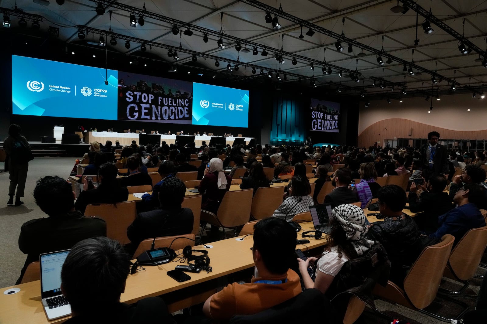 Activists display signs that read "stop fueling genocide" during the People's Plenary at the COP29 U.N. Climate Summit, Thursday, Nov. 21, 2024, in Baku, Azerbaijan. (AP Photo/Rafiq Maqbool)