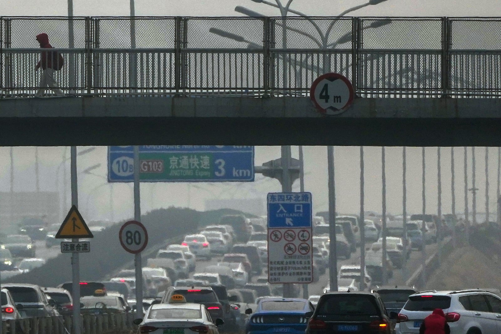 A resident walks across a pedestrian overhead bridge as motorists clogged with heavy traffic on a city highway shrouded with pollution haze in Beijing, Saturday, March 1, 2025. (AP Photo/Andy Wong)