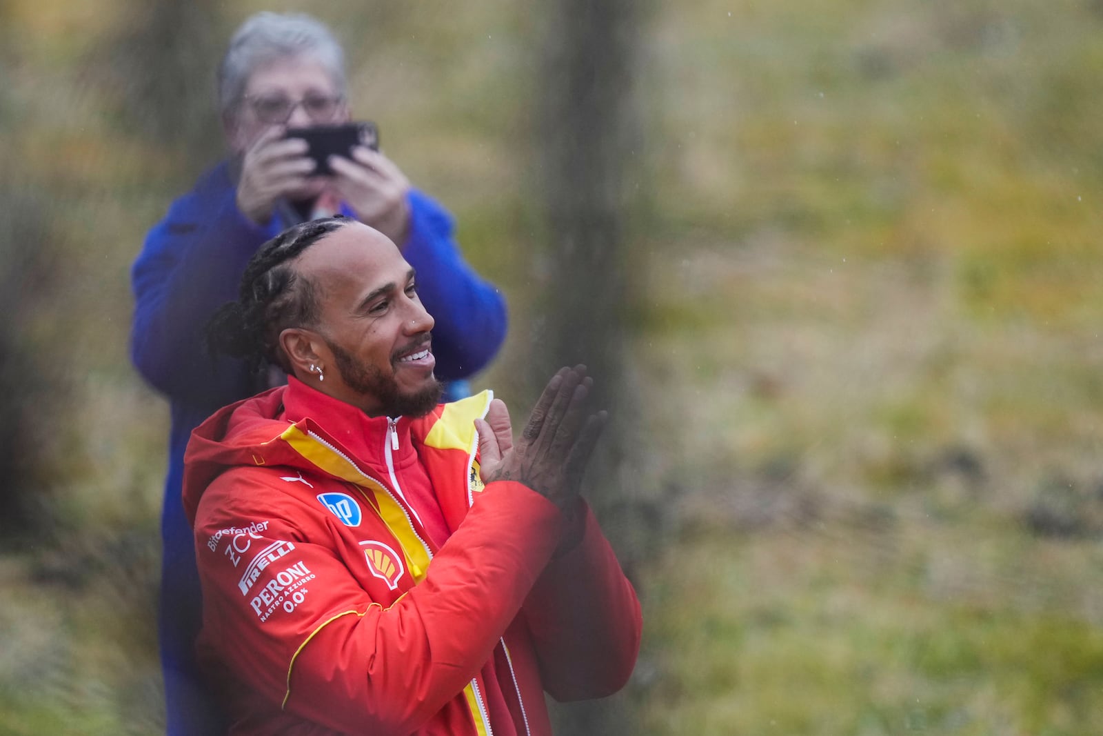 British driver Lewis Hamilton cheers Ferrari fans gathered outside the track, after testing a Ferrari Formula One SF-23, in Fiorano Modenese, Italy, Wednesday, Jan.22, 2025. In background Hamilton's mother Carmen Larbalestier takes pictures with her smartphone. (AP Photo/Luca Bruno)