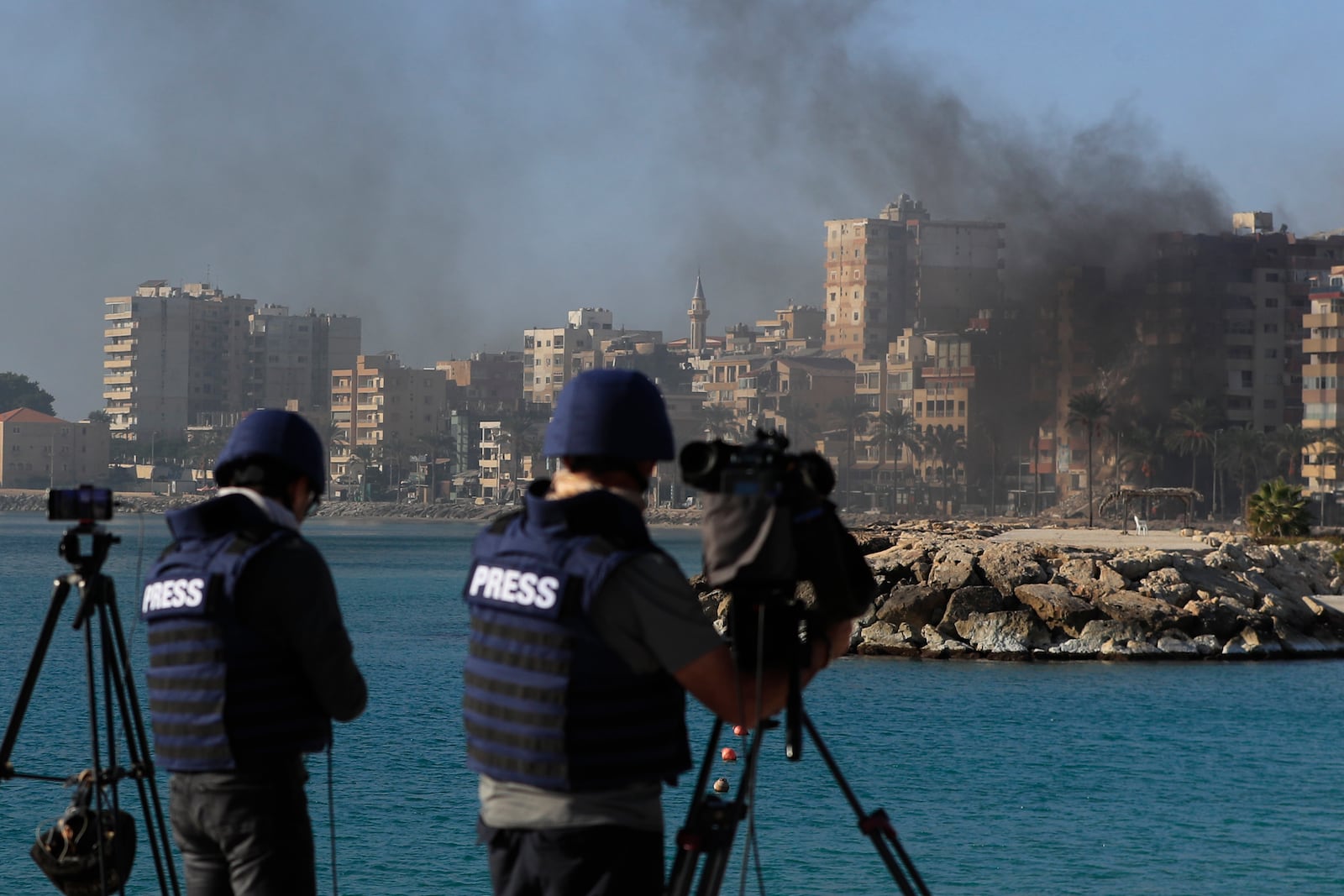 Journalists work as smoke rises from a building hit in an Israeli airstrike in Tyre, southern Lebanon, Monday, Oct. 28, 2024. (AP Photo/Mohammed Zaatari)