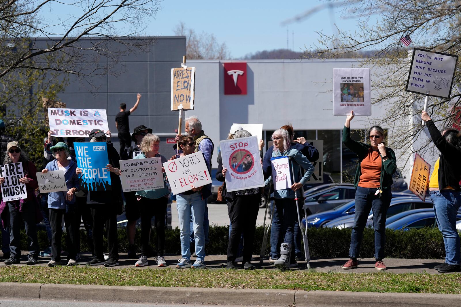 Protesters carrying signs and chant slogans against Elon Musk and President Donald Trump outside a Tesla dealership Saturday, March 22, 2025, in Franklin, Tenn. (AP Photo/George Walker IV)