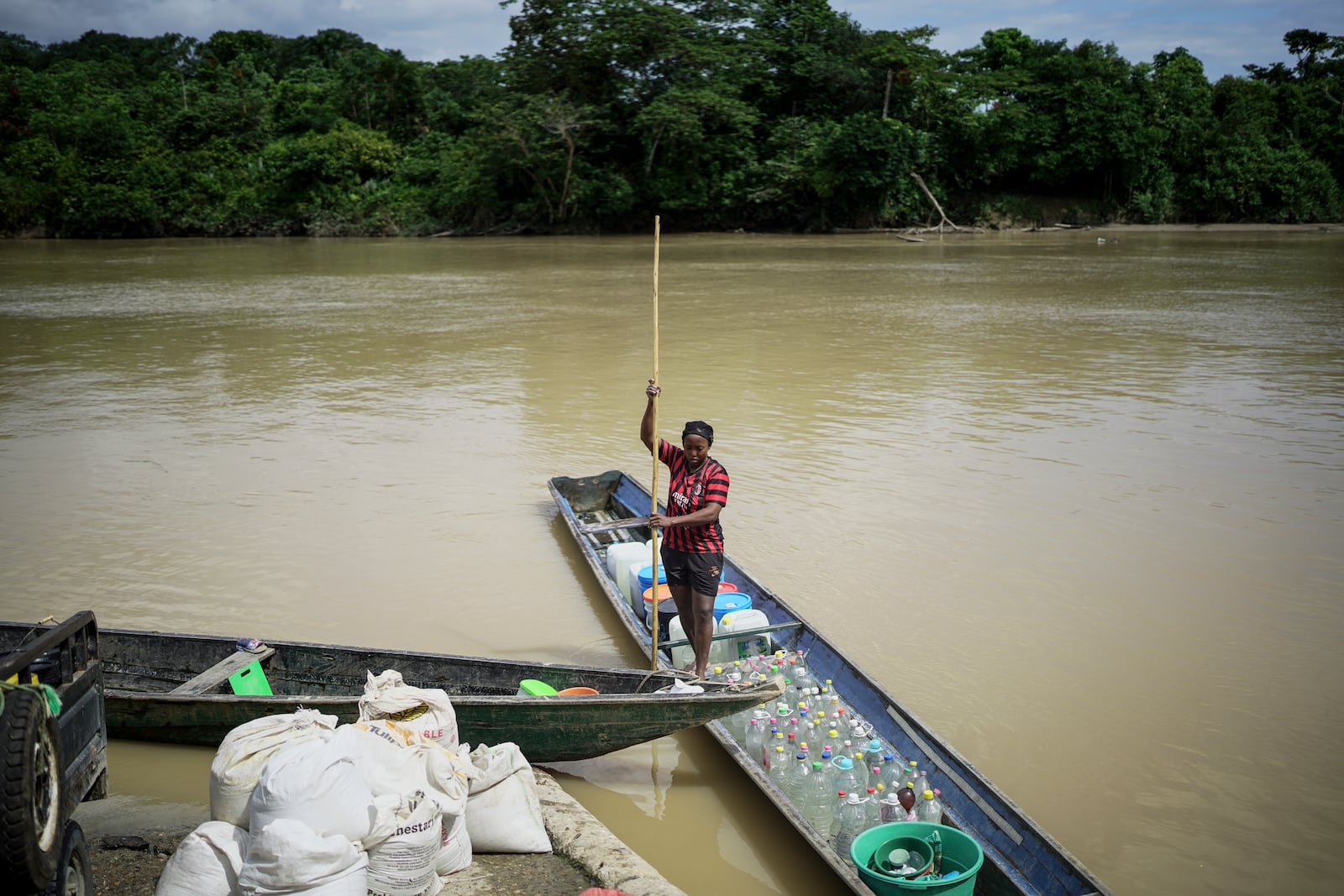 A woman carries bottles to fill them with gasoline to be taken to illegal mining machinery at the Quito River, near Paimado, Colombia, Monday, Sept. 23, 2024. (AP Photo/Ivan Valencia)