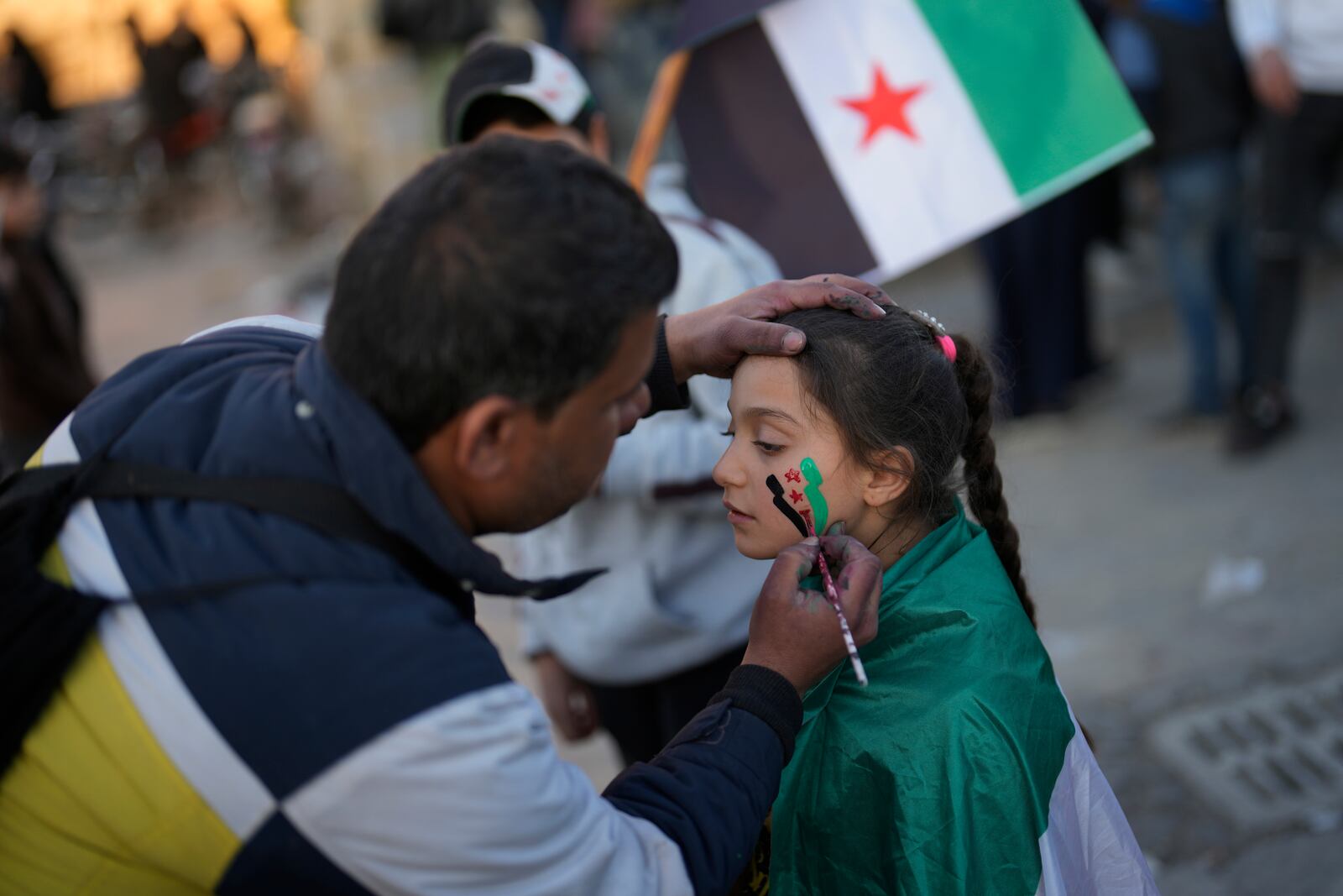 A man draws the "revolutionary" Syrian flag on a girl's face at the ancient Aleppo Citadel in the old city of Aleppo, Syria, Saturday, Dec. 14, 2024. (AP Photo/Khalil Hamra)