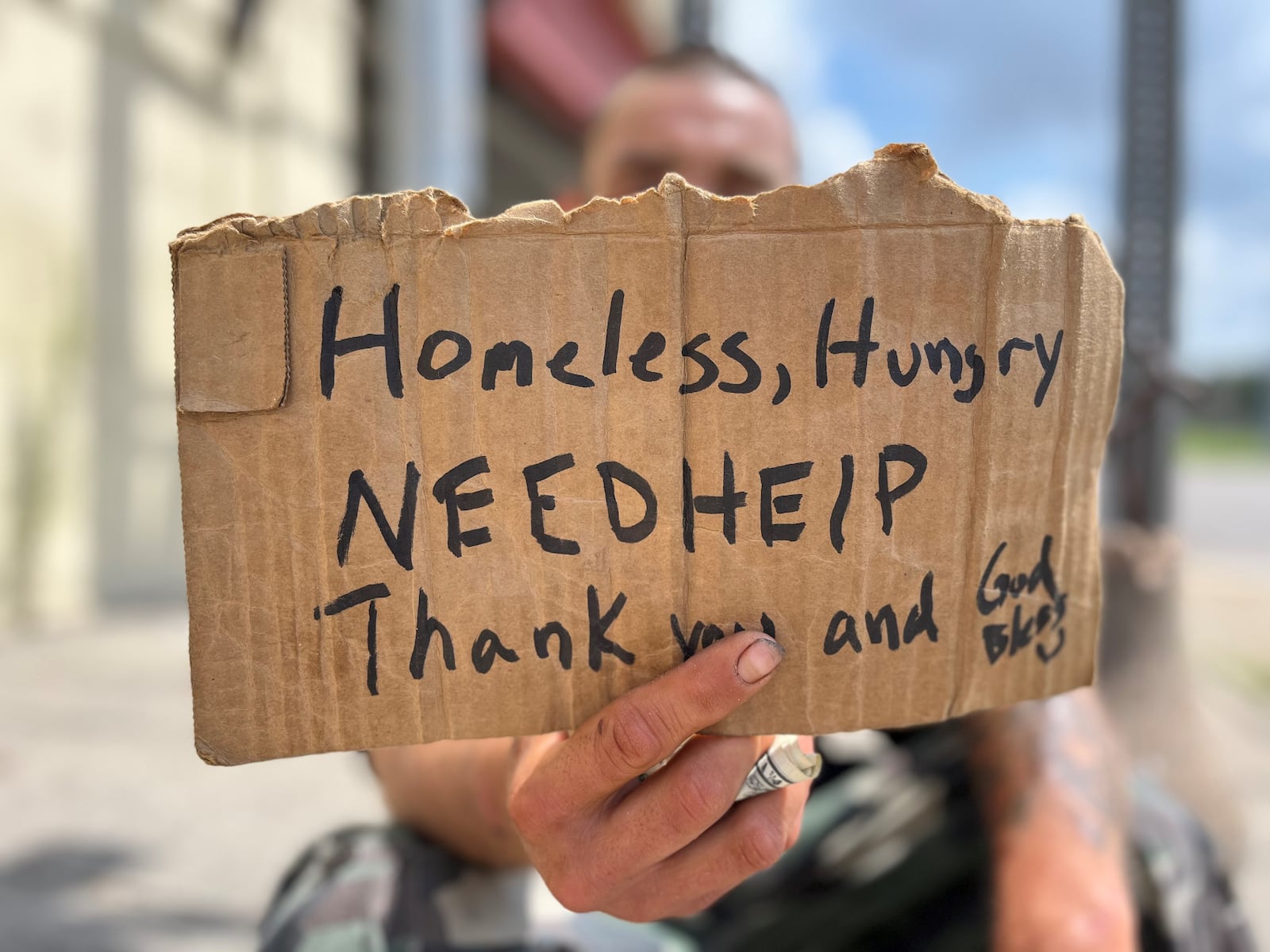 A panhandler holds a sign asking for help near downtown Dayton on July 20, 2023. Dayton is going to launch a new crisis response unit that will help people who struggle with mental and behavioral health issues, likely including homeless individuals. CORNELIUS FROLIK / STAFF