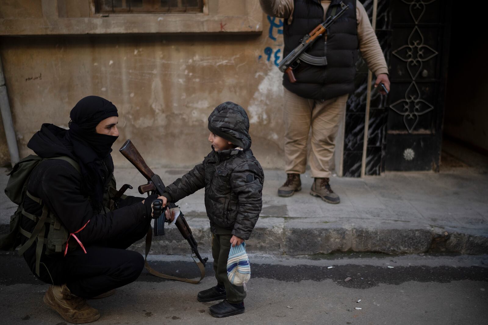 A member of the new security forces shakes hands with a boy during an operation to detain men suspected of being part of militias or loyalist soldiers of the ousted president Bashar Assad in Homs, Syria, Friday, Jan. 3, 2025. (AP Photo/Leo Correa)