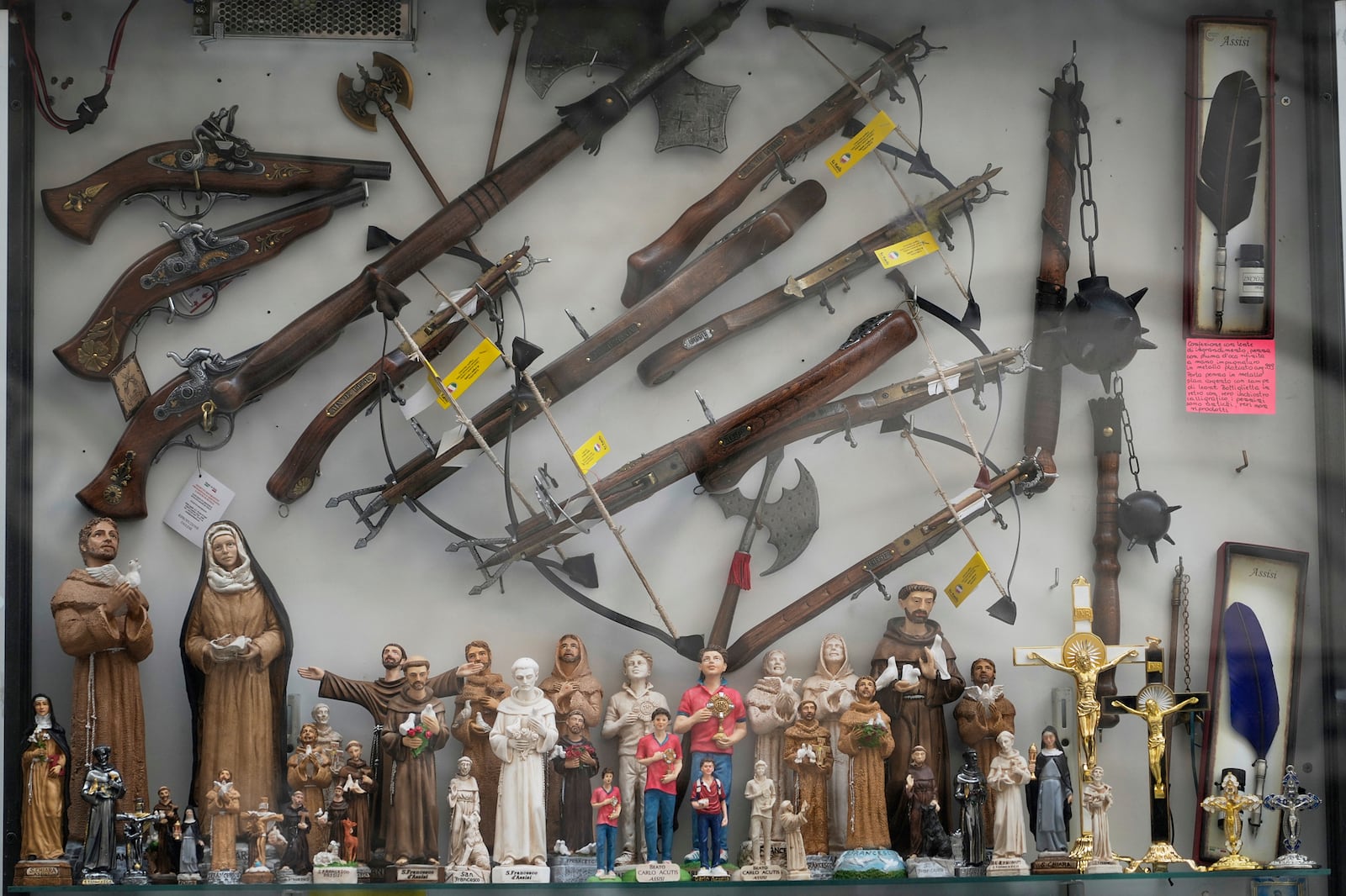 Statuettes of St. Francis and Carlo Acutis are displayed along with replicas of crossbows, pistols and medieval weapons in a shop window in Assisi, Italy, Saturday, March 1, 2025. (AP Photo/Gregorio Borgia)