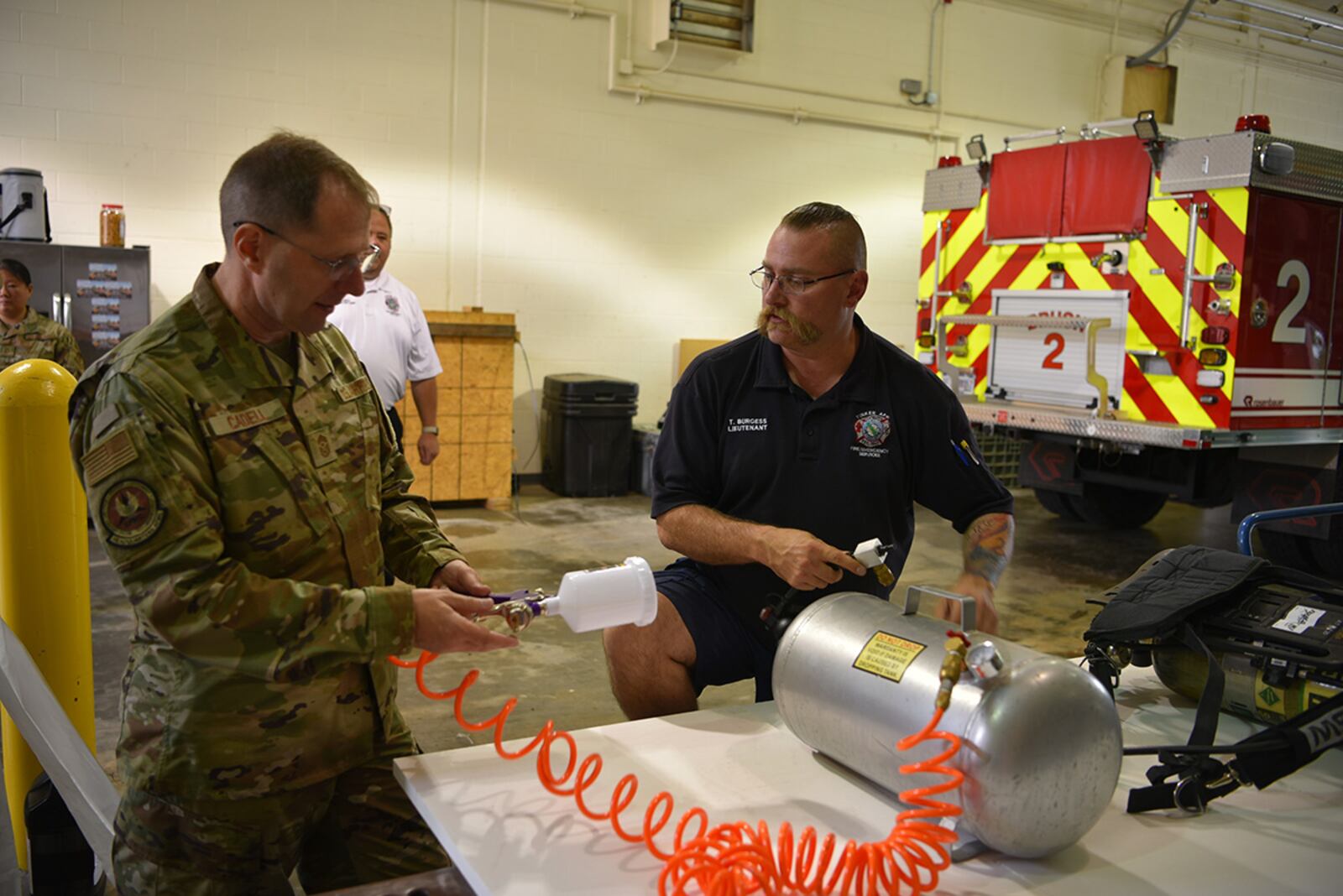 Lt. Tom Burgess (right), Tinker Fire and Emergency Services, shows Chief Master Sgt. Stanley Cadell, command chief, Air Force Materiel Command, a “COVID killer” spraying unit he designed to help sanitize fire trucks and living and office spaces with a low-cost liquid solution he developed. U.S. AIR FORCE PHOTO/RON MULLAN