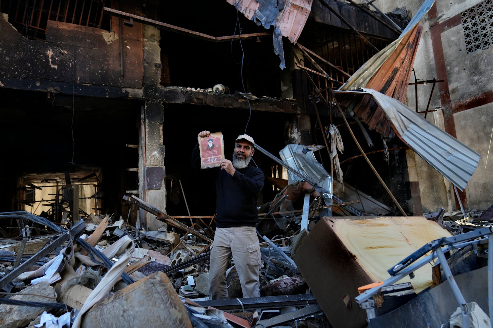 A man holds up a portrait of the late revolutionary founder Ayatollah Khomeini under a destroyed building that was hit by an Israeli airstrike in Dahiyeh, in the southern suburb of Beirut, Lebanon, Monday, Nov. 11, 2024. (AP Photo/Hussein Malla)