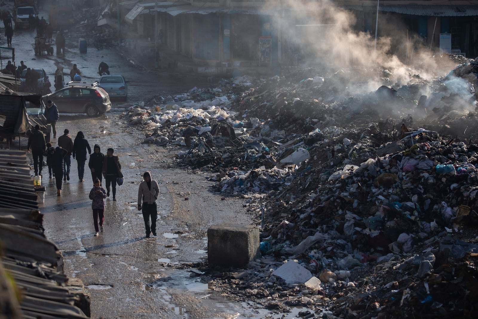 Palestinians walk past a pile of burning garbage, as there is no refuse collection in the city and people are disposing of their rubbish in the streets, in Gaza City, Wednesday, Feb. 12, 2025. (AP Photo/Jehad Alshrafi)