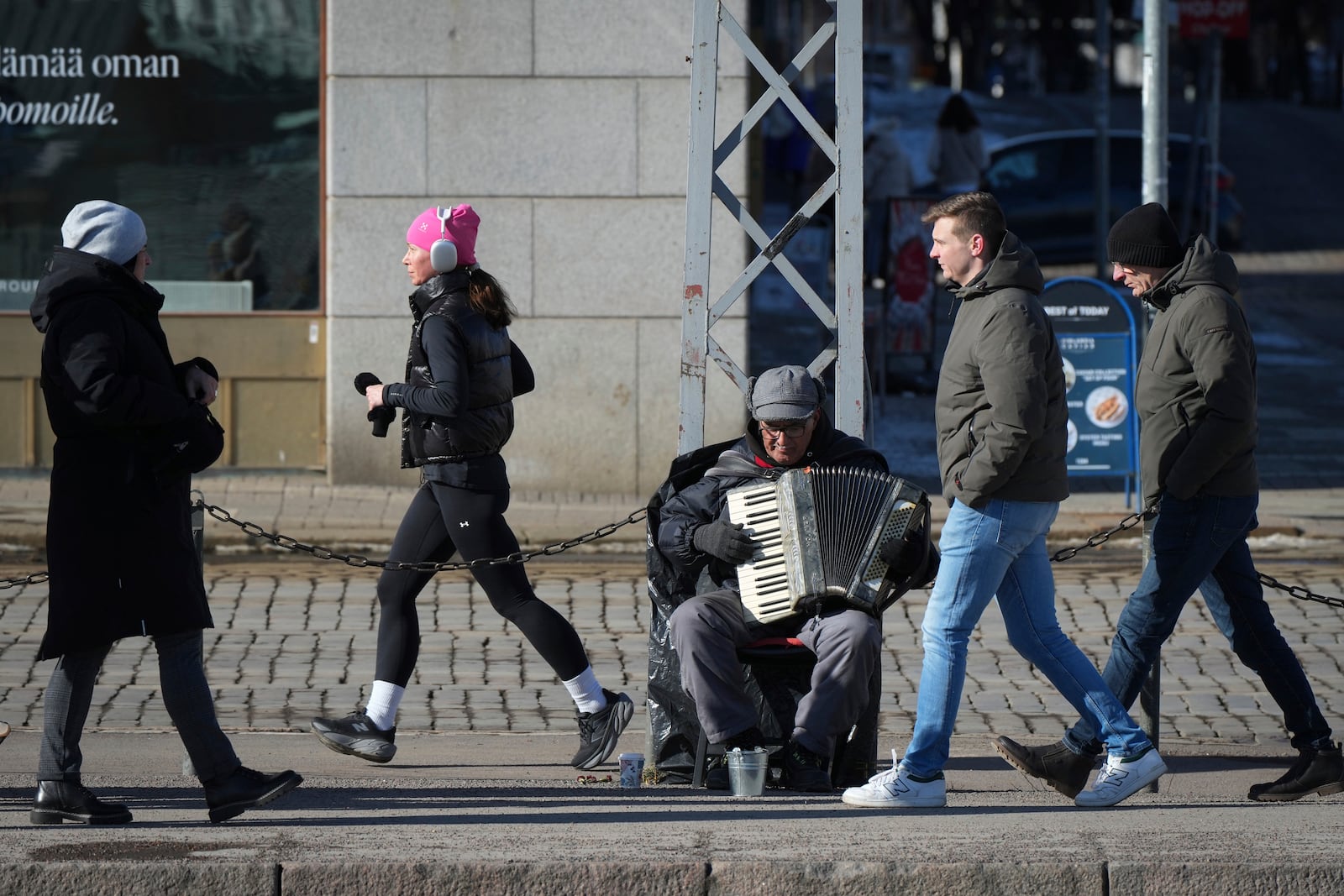 People walk past a street musician in the center of Helsinki, Finland, Saturday, March 15, 2025. (AP Photo/Sergei Grits)