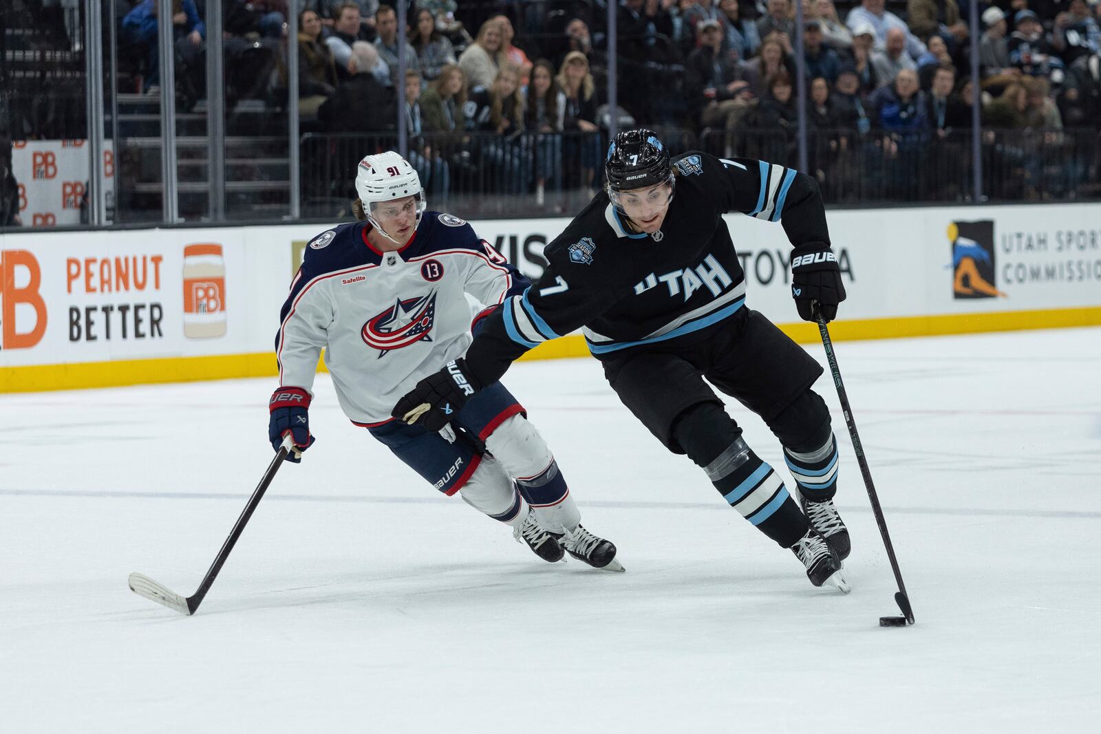 Utah Hockey Club defenseman Michael Kesselring (7) skates with the puck against Columbus Blue Jackets center Kent Johnson (91) during the first period of an NHL hockey game Friday, Jan. 31, 2025, in Salt Lake City. (AP Photo/Melissa Majchrzak)