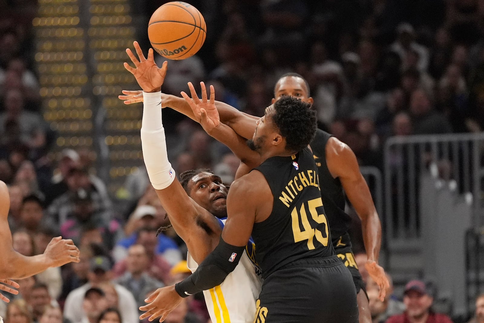 Golden State Warriors forward Kevon Looney, left, and Cleveland Cavaliers guard Donovan Mitchell (45) reach for the ball in the first,half of an NBA basketball game, Friday, Nov. 8, 2024, in Cleveland. (AP Photo/Sue Ogrocki)