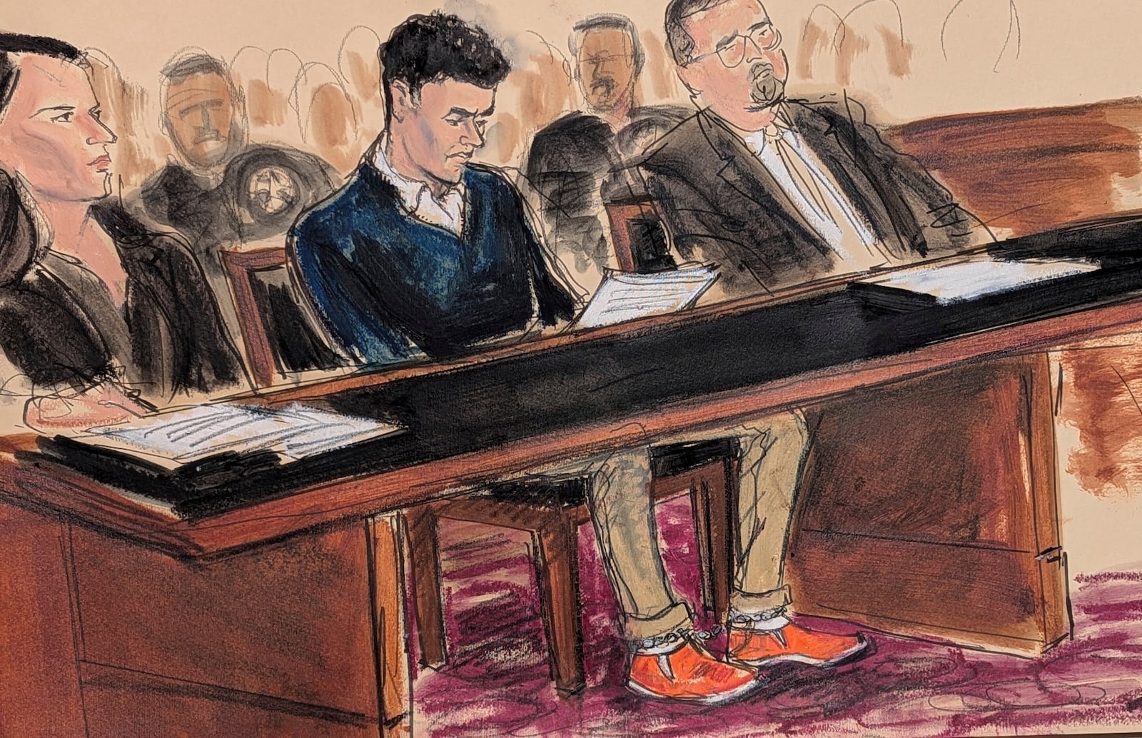 Luigi Mangione, center, sits in court reading the federal complaint while wearing orange slip on shoes and his ankles shackled in Manhattan federal court, Thursday, Dec. 19, 2024, in New York. . He is flanked by his attorneys, Karen Agnifilo, left, and Marc Agnifilo. (Elizabeth Williams via AP)