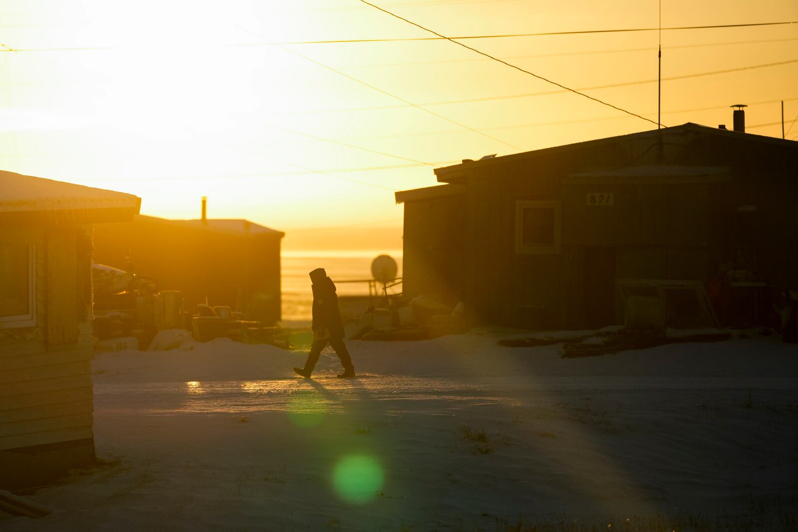 The sun rises over the village as a resident walks on a snowy road in Kaktovik, Alaska, Tuesday, Oct. 15, 2024. (AP Photo/Lindsey Wasson)