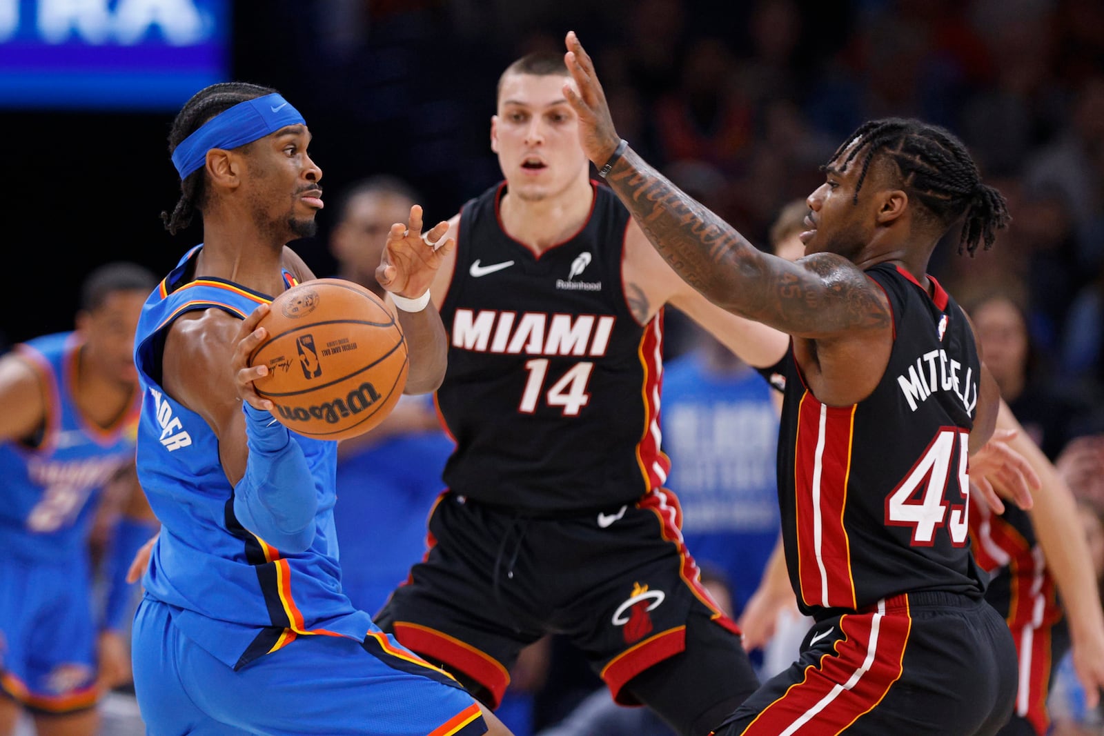 Oklahoma City Thunder guard Shai Gilgeous-Alexander, left, passes the ball away from Miami Heat guards Tyler Herro (14) and Davion Mitchell (45) during the first half of an NBA basketball game Wednesday, Feb. 12, 2025, in Oklahoma City. (AP Photo/Nate Billings)