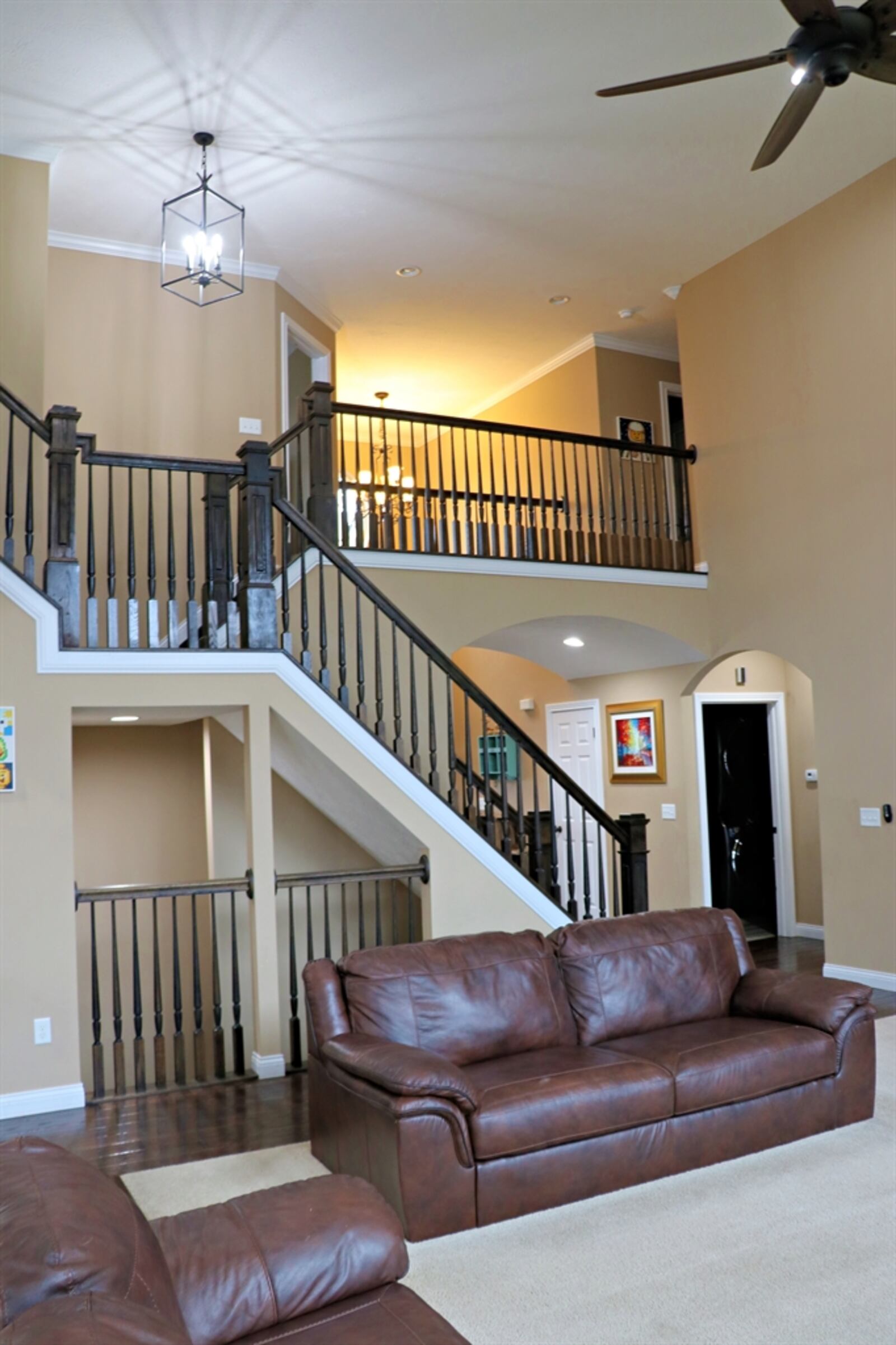 Opposite a fireplace, the open staircase has rich stained-wood banisters and railings that ascend to a landing where there is a lighted artwork nook.