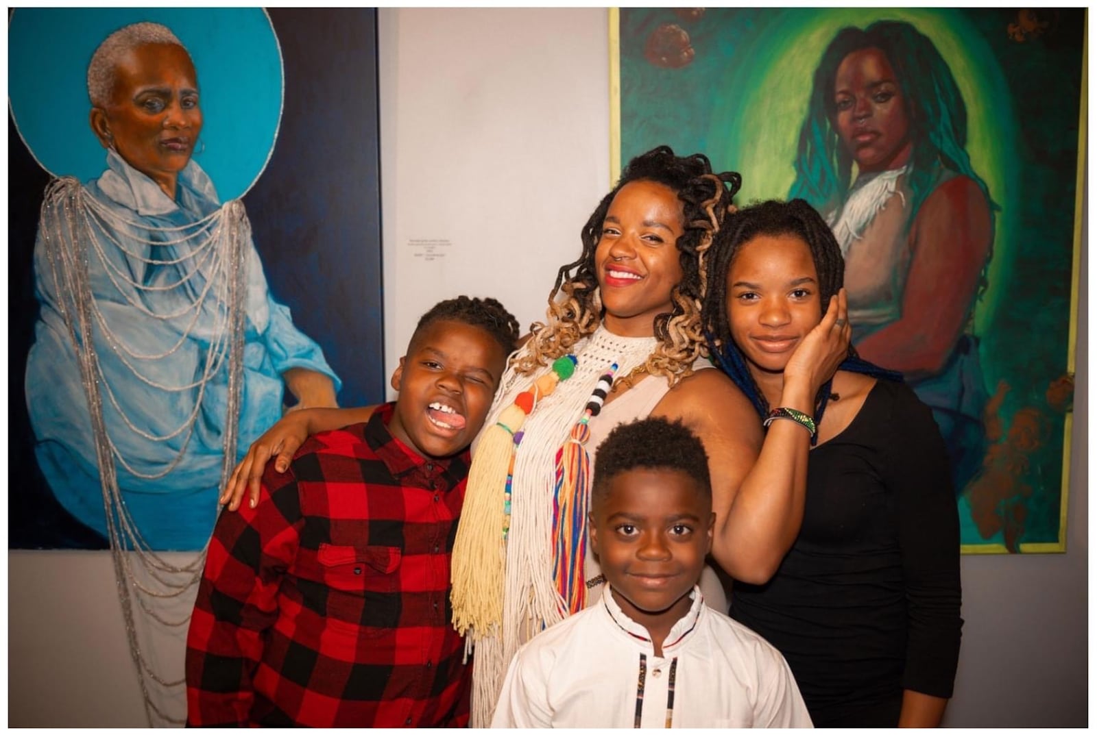 Artist and Professor Erin M. Smith stands with her children in front of her paintings at solo exhibition "HAIR-itage."