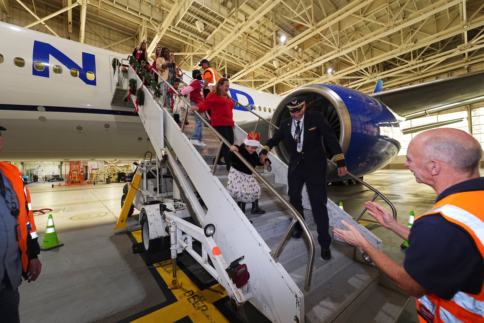 Captain Paul Purkey helps a participant navigate the stairs during the United Airlines annual "fantasy flight" to a fictional North Pole at Denver International Airport, Saturday, Dec. 14, 2024, in Denver. (AP Photo/David Zalubowski)