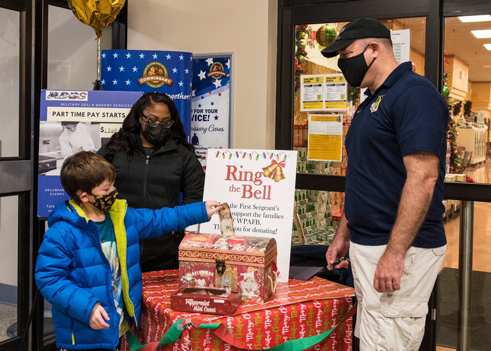 Col. Patrick Miller, 88th Air Base Wing and installation commander, and Senior Airman Andaiyé Broussard-Marion watch as Parker Fogg donates to the First Sergeants Council’s “Ring the Bell” campaign Dec. 11 at Wright-Patterson Air Force Base. U.S. AIR FORCE PHOTO/JAIMA FOGG