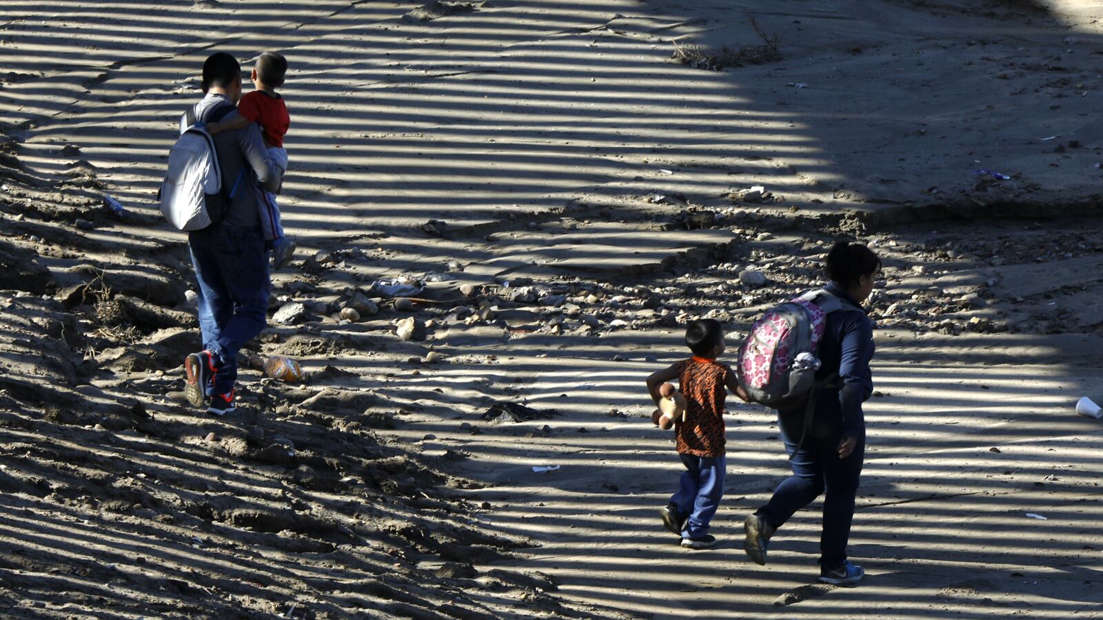 A migrant family walks in the shadow of the U.S. border wall Dec. 9, 2018, near Imperial Beach, California, after squeezing through a hole along the border with Tijuana, Mexico. Discouraged by the long wait to apply for asylum through official ports of entry, many Central American migrants are choosing to cross the border wall illegally and hand themselves over to Border Patrol agents to begin the application process.