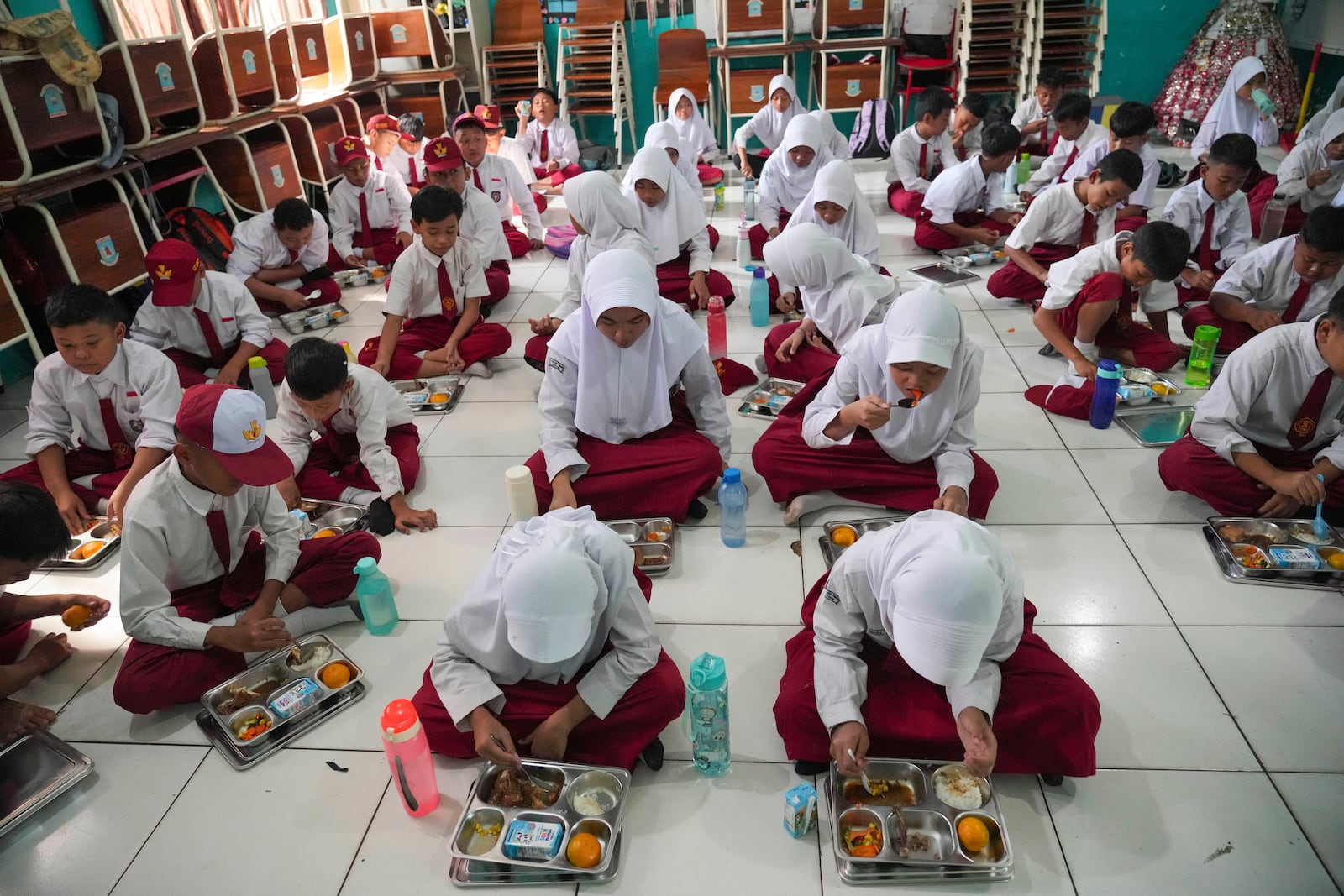 Students sit on the floor as they have their meals during the kick off of President Prabowo Subianto's ambitious free meal program to feed children and pregnant women nationwide despite critics saying that its required logistics could hurt Indonesia's state finances and economy, at an elementary school in Banten, Indonesia, Monday, Jan. 6, 2025. (AP Photo/Tatan Syuflana)