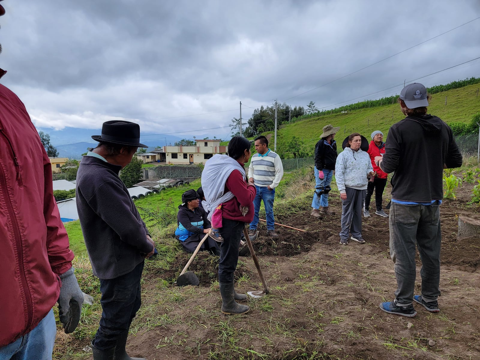 Waiting on instructions prior to planting; the lady in the red shirt with the white cloth on her back is carrying her baby while she works.