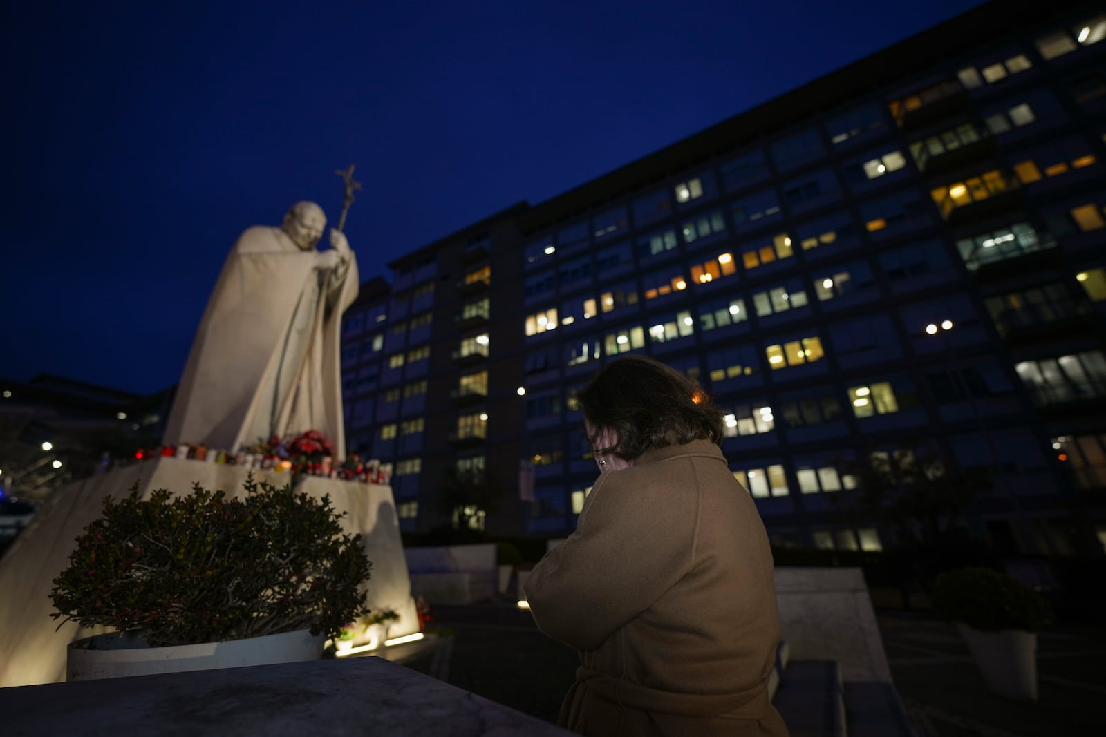 A woman prays in front of a statue of Pope John Paul II in front of the Agostino Gemelli Polyclinic, Rome, Wednesday, Feb. 19, 2025, where the Pontiff is hospitalized since Friday, Feb. 14. (AP Photo/Andrew Medichini)