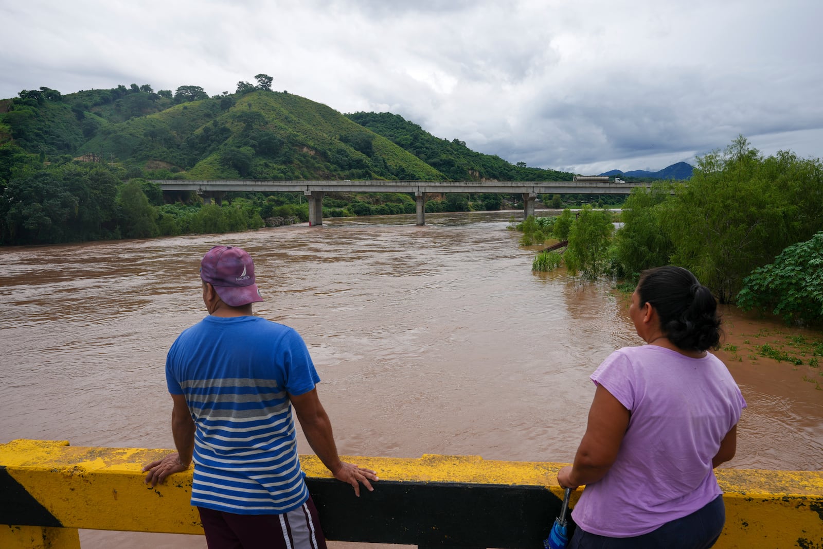 People standing on a bridge to watch the overflowing Ulúa River after Tropical Storm Sara, in Potrerillos, Honduras, Sunday, Nov. 17, 2024. (AP Photo/Moises Castillo)