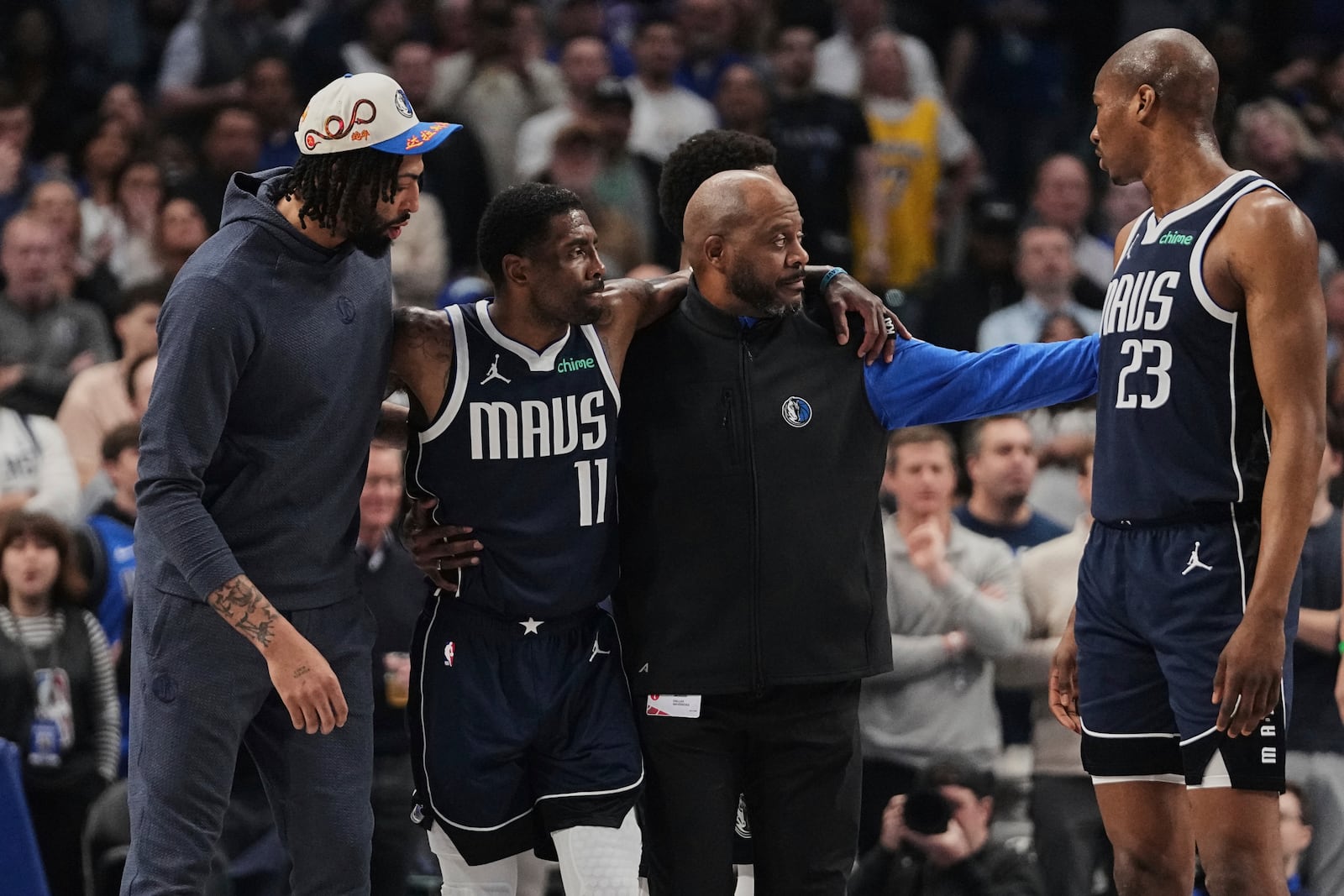 Dallas Mavericks' Anthony Davis, left, and a staff member, right, assist Kyrie Irving (11) off the court after he suffered an unknown injury in the first half of an NBA basketball game against the Sacramento Kings in Dallas, Monday, March 3, 2025. (AP Photo/Tony Gutierrez)