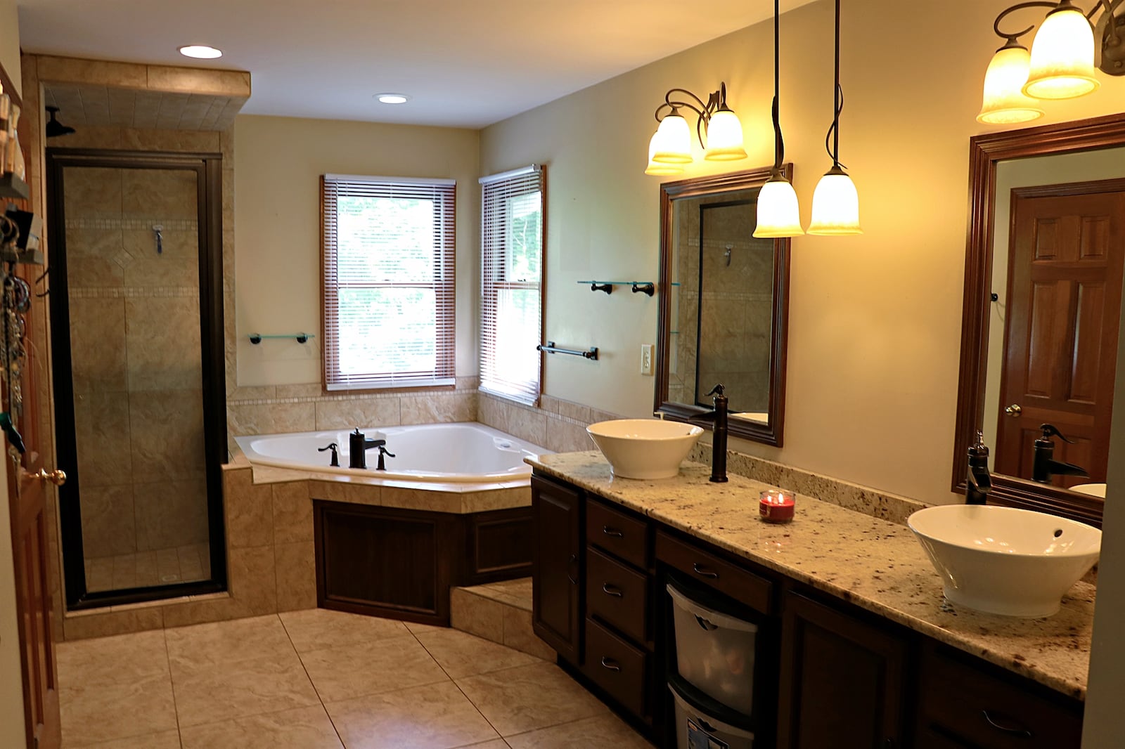 The primary bath has a long vanity with two bowl sinks. A corner whirlpool tub is below two windows and has ceramic-tile surround. 