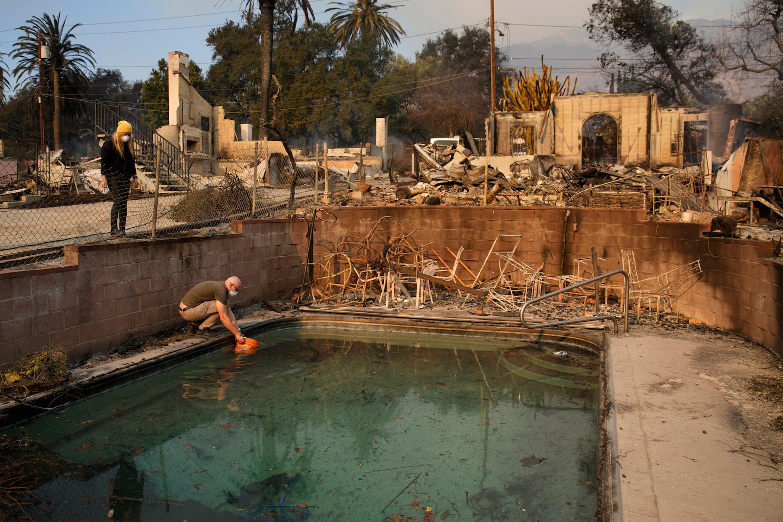 Robert Karban fills a bucket with water from a swimming pool to put out hot spots at a home destroyed by the Eaton fire, Thursday, Jan. 9, 2025, in Altadena, Calif. (AP Photo/John Locher)