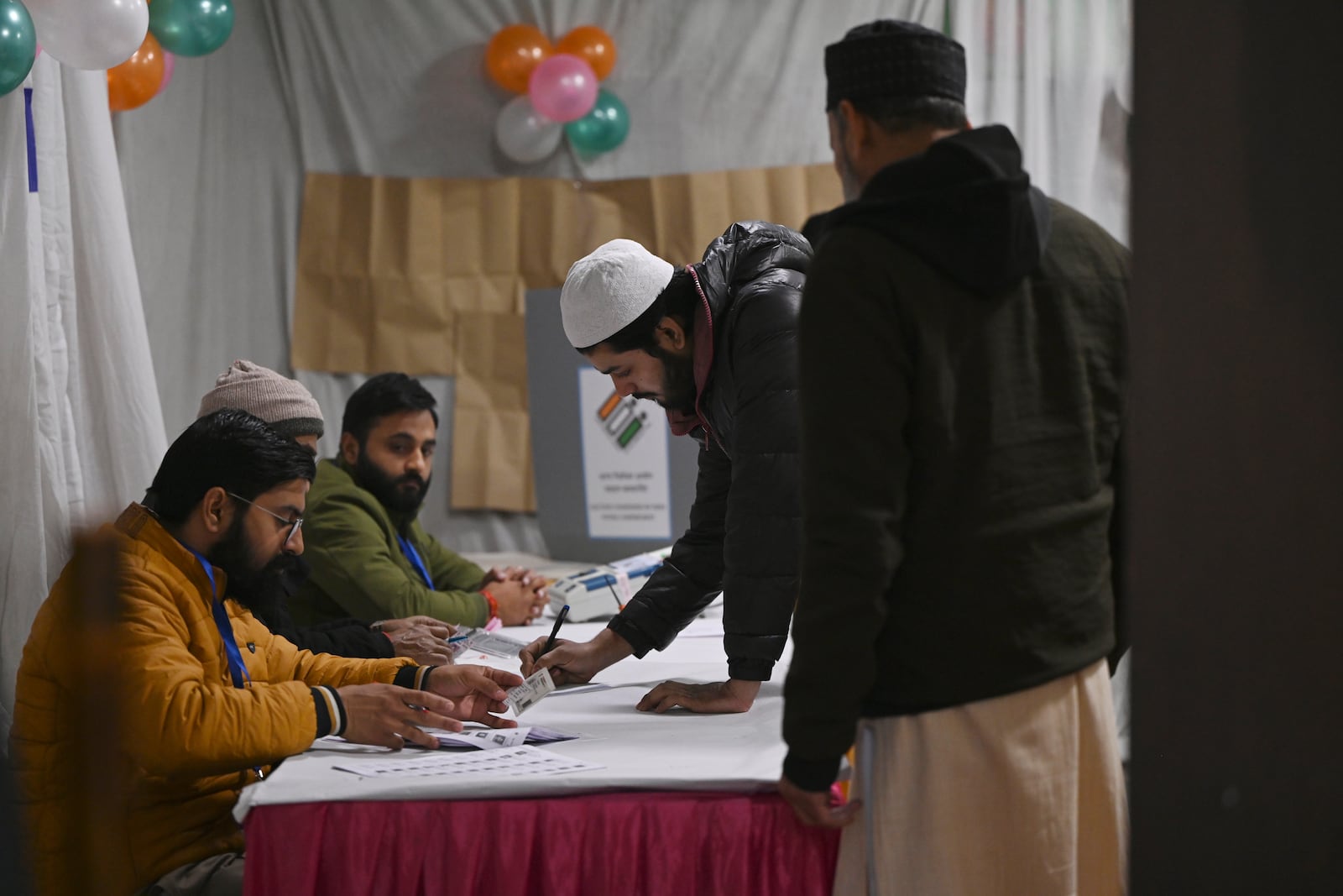 A Muslim man signs to take a voting slip for casting his vote for Delhi state election at a polling booth in New Delhi, India, Wednesday, Feb. 5, 2025. (AP Photo)