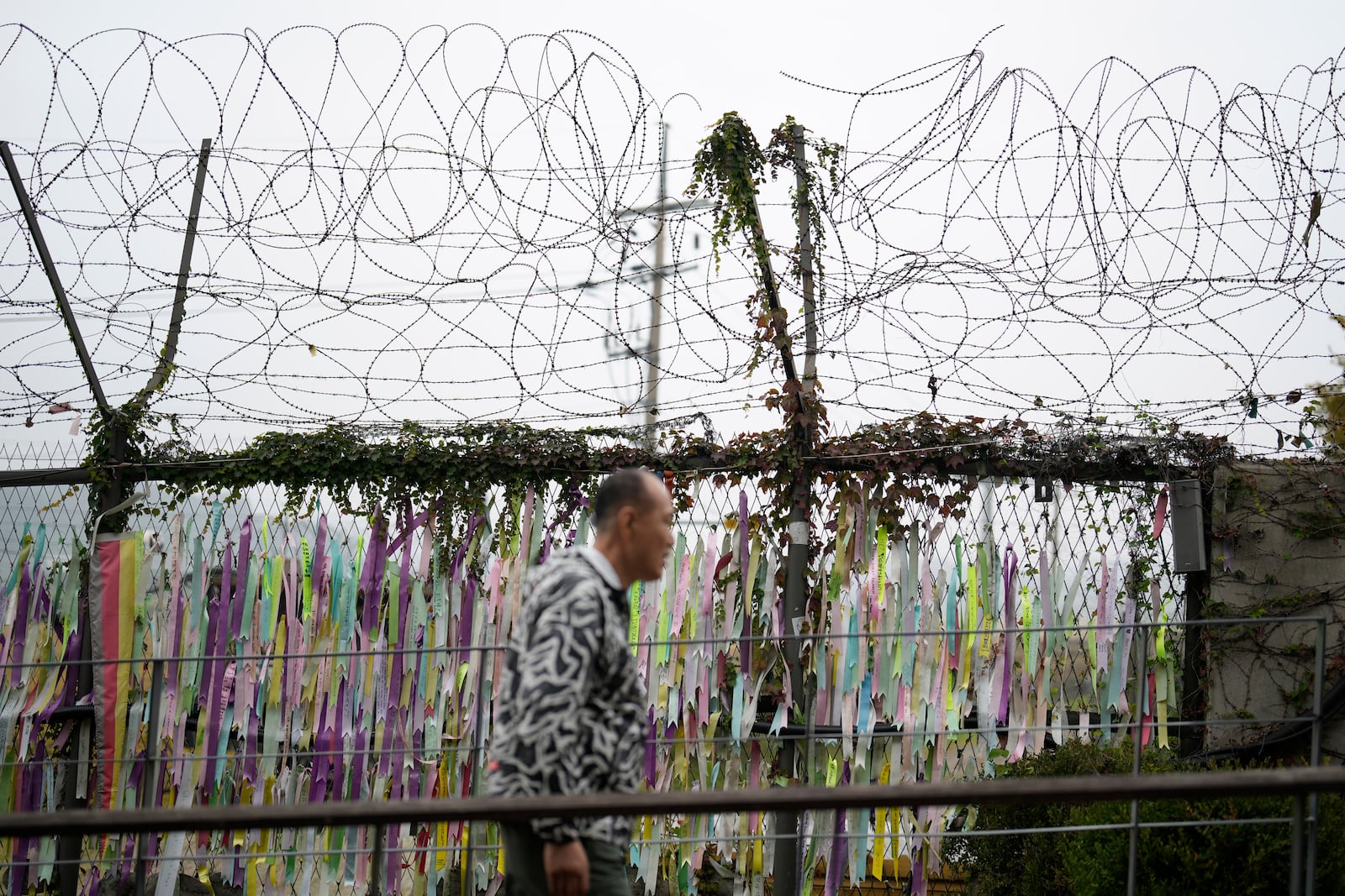 A visitor walks near a wire fence decorated with ribbons written with messages wishing for the reunification of the two Koreas at the Imjingak Pavilion in Paju, South Korea, Tuesday, Oct. 15, 2024. (AP Photo/Lee Jin-man)