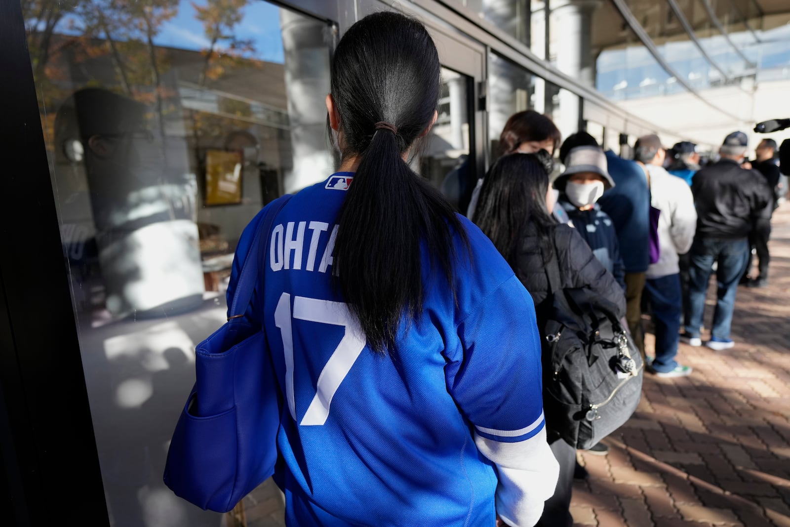 A woman wearing a baseball jersey of Shohei Ohtani of the Los Angeles Dodgers and others wait in line to watch a live stream of Game 3 of the baseball World Series between the Los Angeles Dodgers and the New York Yankees, in a public viewing event in Oshu, northeastern Japan, the hometown of Ohtani, Tuesday,Oct. 29, 2024. (AP Photo/Eugene Hoshiko)