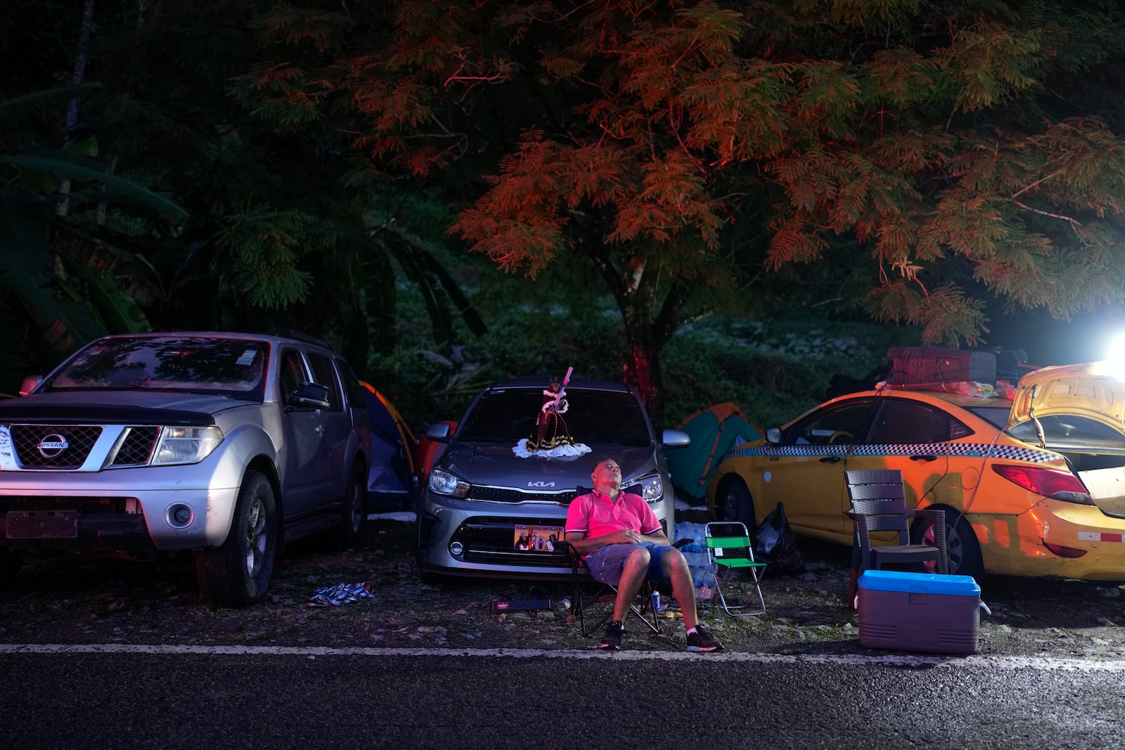 A pilgrim rests next to a replica of the Black Christ sitting on a car hood in Portobelo, Panama, Monday, Oct. 21, 2024, during a festival celebrating the iconic statue that was found on the shore in 1658. (AP Photo/Matias Delacroix)