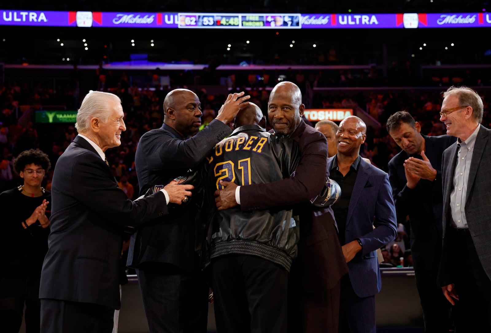 Former Los Angeles Lakers player Michel Cooper, center, is mobbed by coach Pat Riley, left, Magic Johnson, James Worthy, Byron Scott, Vlade Divac and Kurt Rambis after his jersey was retired during a ceremony during halftime in an NBA basketball game between Los Angeles Lakers and the San Antonio Spurs, Monday, Jan. 13, 2025, in Los Angeles. (AP Photo/Kevork Djansezian)