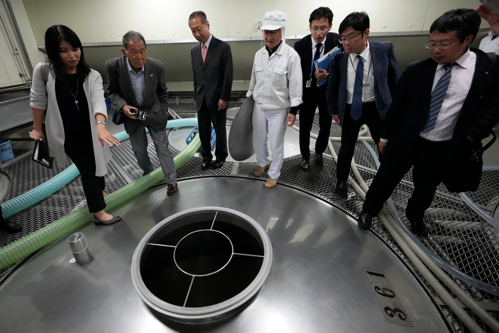 An interpreter, left, translates for Junichiro Ozawa, head of Ozawa Sake Brewery, third left, and his worker (in white) as Hitoshi Utsunomiya, far right, director of the Japan Sake and Shochu Makers Association, stands during a media tour at the brewery in Ome, on the western outskirts of Tokyo, Japan, Wednesday, Nov. 13, 2024. (AP Photo/Hiro Komae)