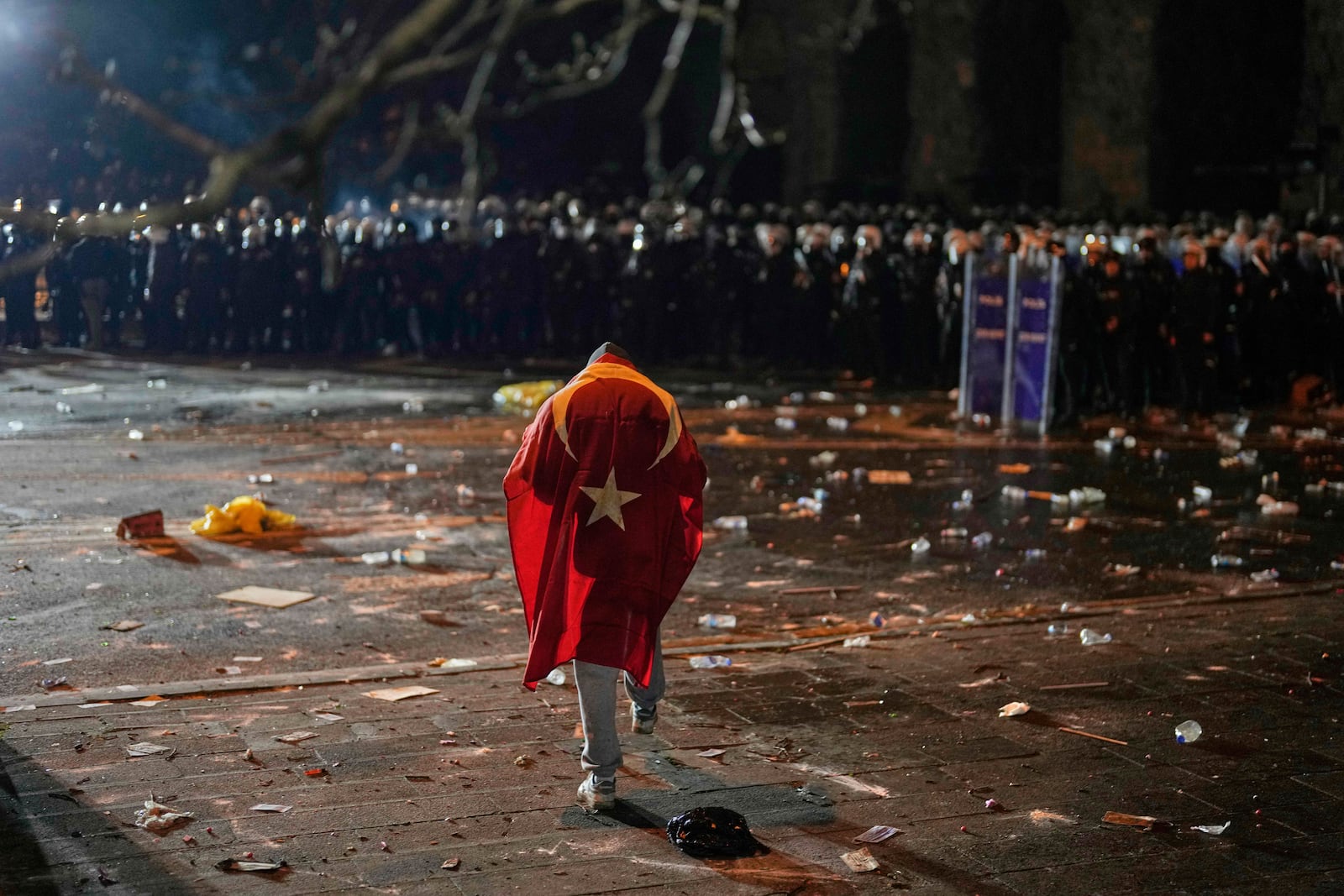 A man with the Turkish flag on his back stands in front of anti riot police officers during clashes in a rally against the arrest of Istanbul's Mayor Ekrem Imamoglu, in Istanbul, Turkey, Friday, March 21, 2025. (AP Photo/Khalil Hamra)