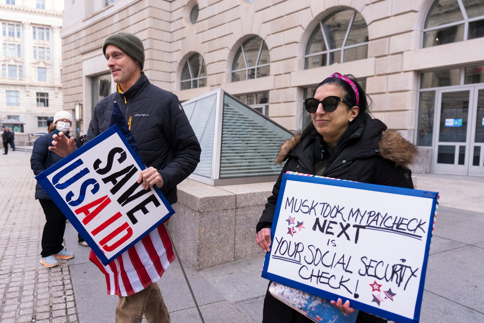 United States Agency for International Development, or USAID contract worker Priya Kathpal, right, and Taylor Williamson, left, who works for a company doing contract work for USAID, carry signs outside the USAID headquarters in Washington, Monday, Feb. 10, 2025. (AP Photo/Manuel Balce Ceneta)