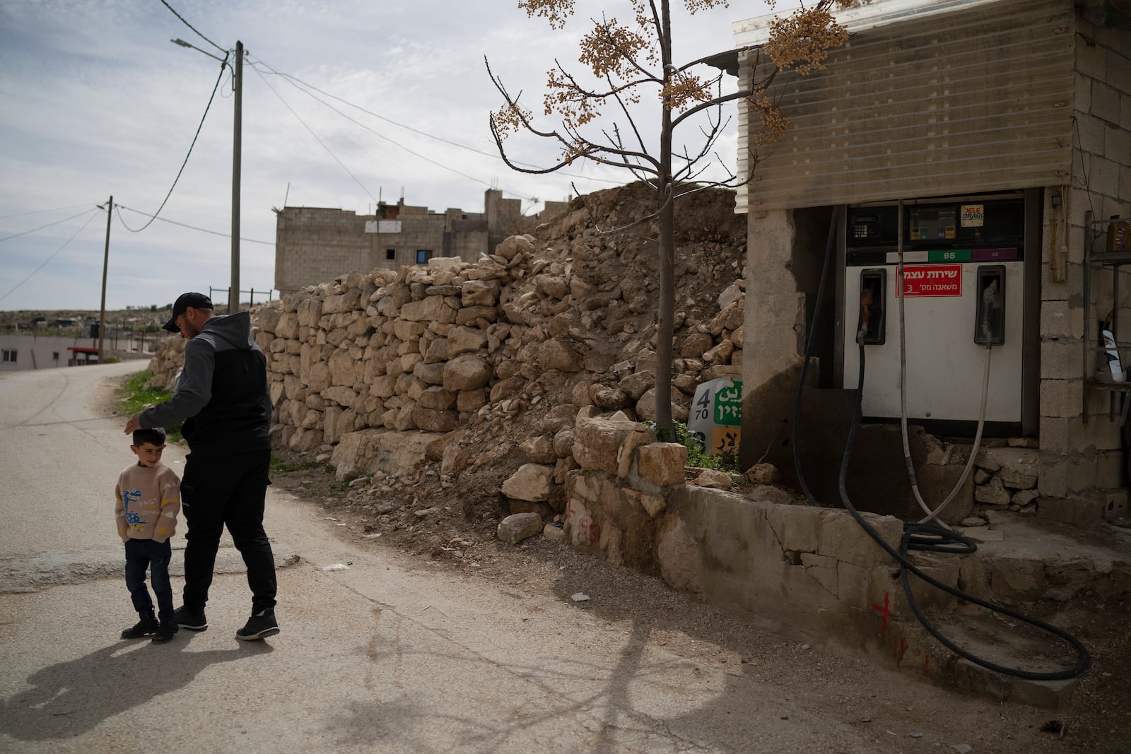 Salem Adra, walks with his 4-year-old son Elias, past his family's gas station, featured in the Oscar-winning documentary "No Other Land," co-directed by his brother Palestinian activist Basel Adra, at the West Bank village of Tuwani, Monday, March 3, 2025. (AP Photo/Leo Correa)