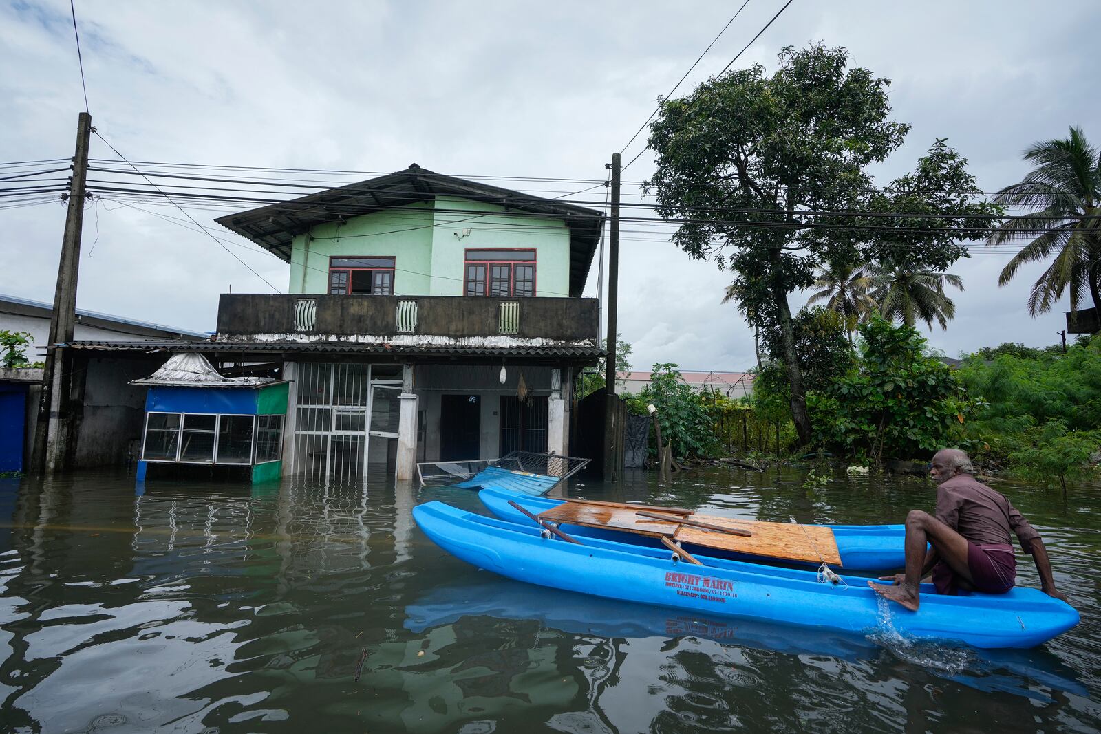 A man sits on a catamaran next to a damaged house in a flooded area in Colombo, Sri Lanka, Monday, Oct. 14, 2024. (AP Photo/Eranga Jayawardena)