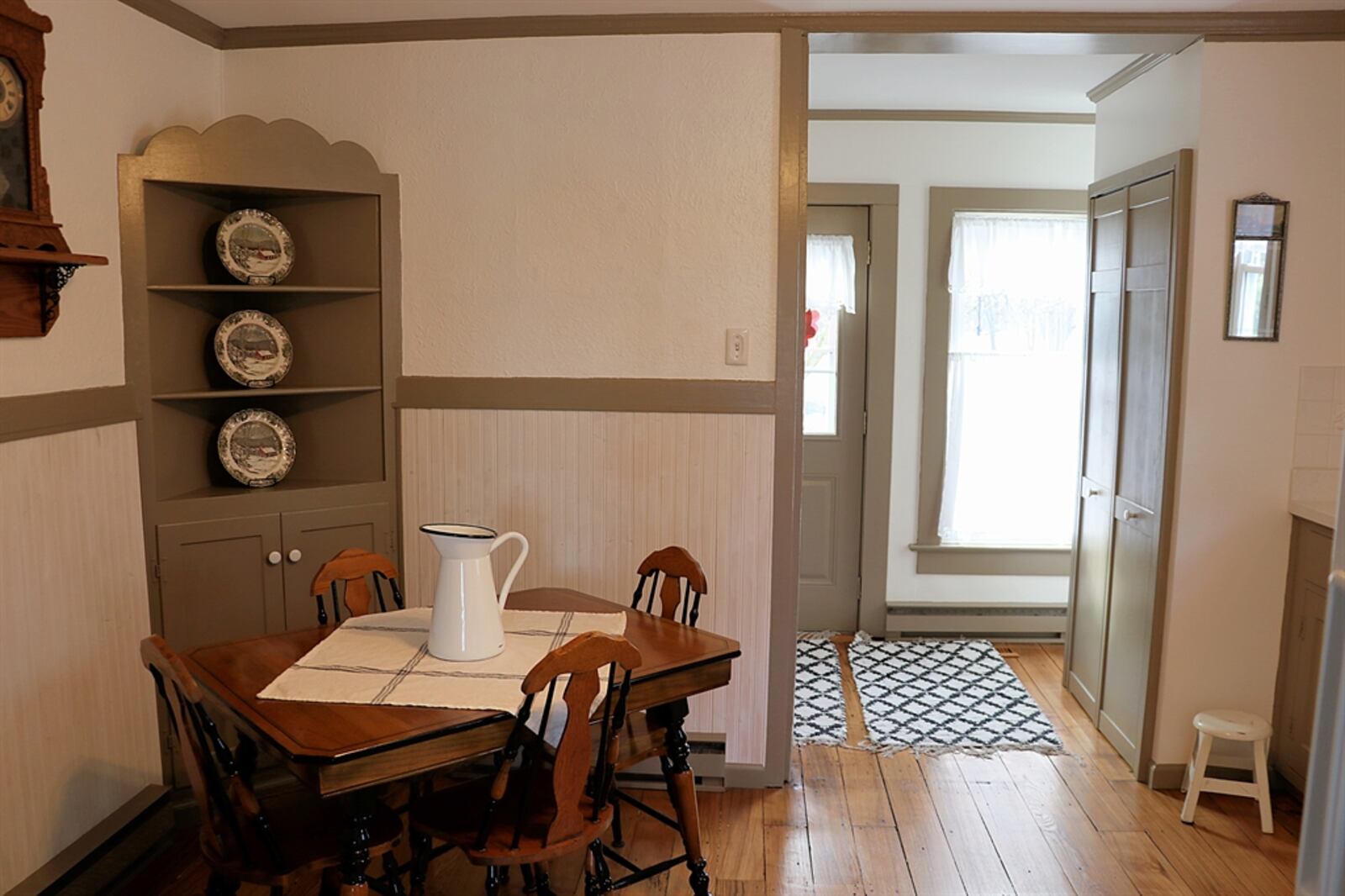 The kitchen has shiplap wall treatments that surround a corner hutch within the breakfast space. Original cabinetry has been painted to complement the light wall and trim. A solid-surface counter includes a double sink that is below a window.