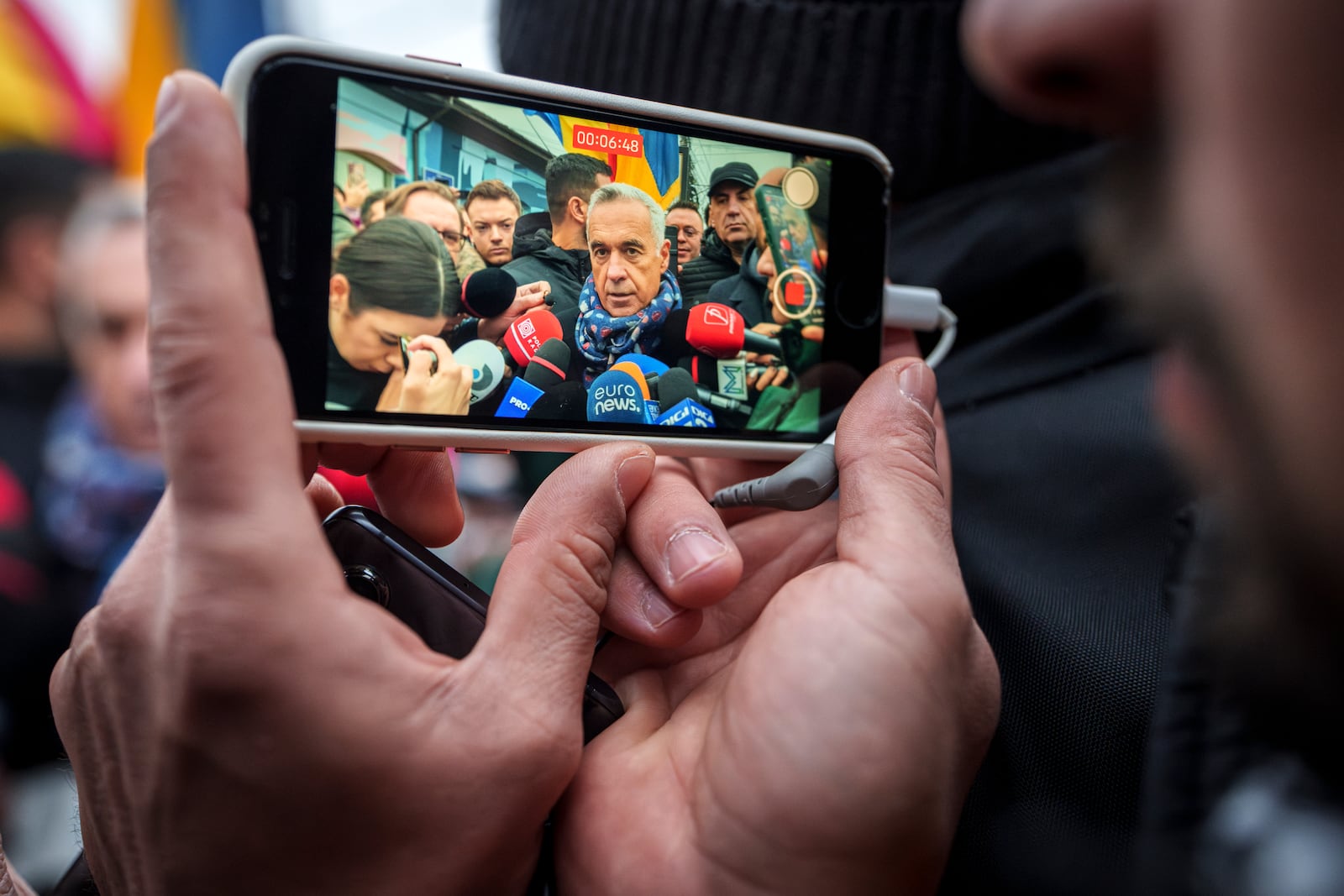 A man records video of Calin Georgescu, an independent candidate for president who won the first round of presidential elections, speaking to media outside a closed voting station after Romania's Constitutional Court annulled the first round of presidential elections, in Mogosoaia, Romania, Sunday, Dec. 8, 2024. (AP Photo/Vadim Ghirda)