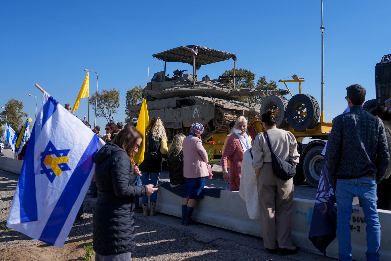 Israelis waiting on the side of a road where the funeral convoy carrying the coffins of slain hostages Shiri Bibas and her two children, Ariel and Kfir, will pass by near Kibbutz Nir Oz, Israel, Wednesday, Feb. 26, 2025. The mother and her two children were abducted by Hamas on Oct. 7, 2023, and their remains were returned from Gaza to Israel last week as part of a ceasefire agreement with Hamas. (AP Photo/Ohad Zwigenberg)