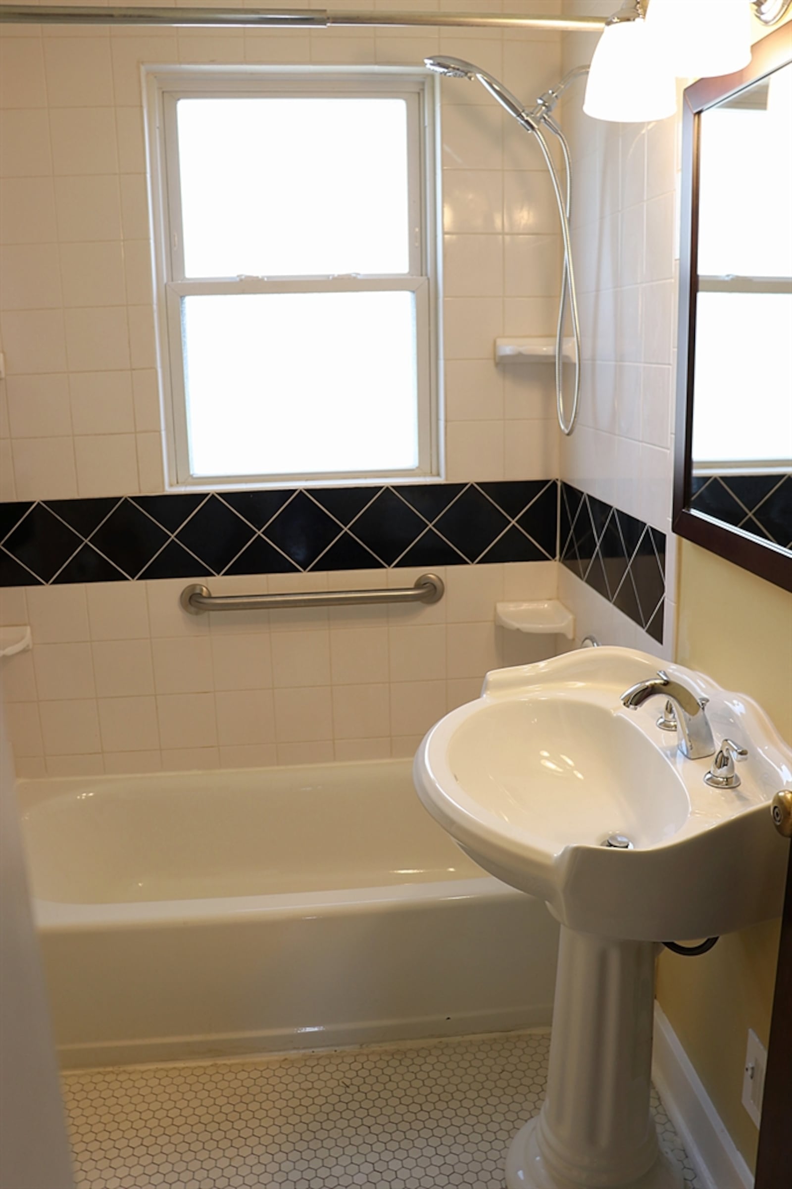 The bathroom has a pedestal sink with an updated mirror and light fixture. 