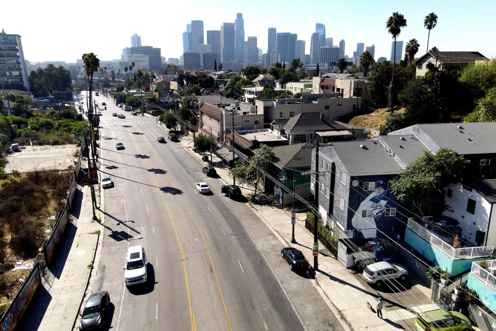 A person, bottom right, walks a dog on Sunset Boulevard near a building donning a mural depicting former Los Angeles Dodgers pitcher Fernando Valenzuela, Wednesday, Oct. 23, 2024, in Los Angeles. Valenzuela, the Mexican-born phenom for the Los Angeles Dodgers who inspired "Fernandomania" while winning the NL Cy Young Award and Rookie of the Year in 1981, died Tuesday, Oct. 22, 2024. (AP Photo/Julio Cortez)