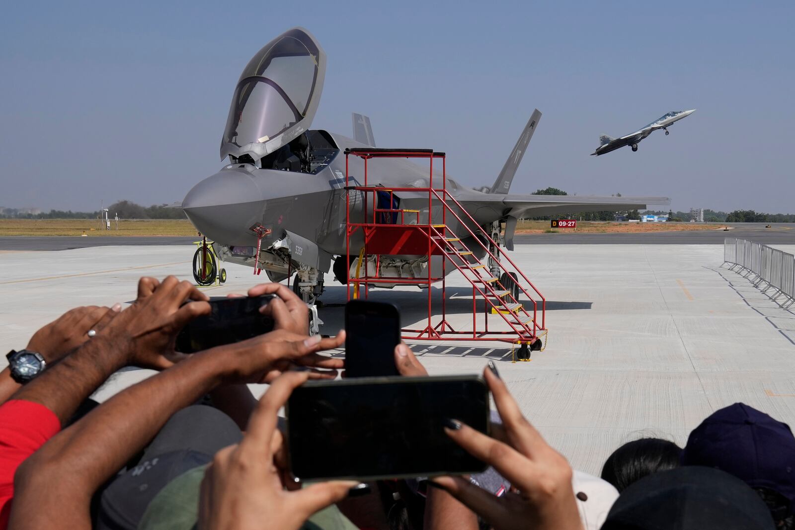 Visitors take pictures as Russia's Su-57 fighter aircraft takes off behind the U.S. Air Force fighter aircraft F-35, parked at the static display area, on the last day of the Aero India 2025, a biennial event, at Yelahanka air base in Bengaluru, India, Friday, Feb. 14, 2025. (AP Photo/Aijaz Rahi)