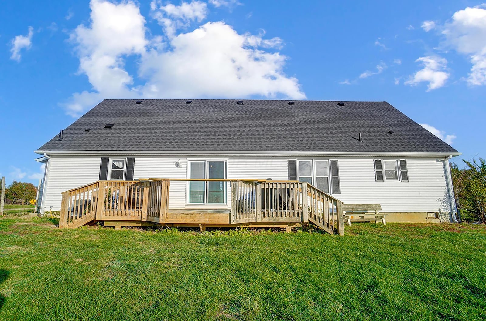 The rear of the home has a wood deck with railings and overlooks the open, flat lot.